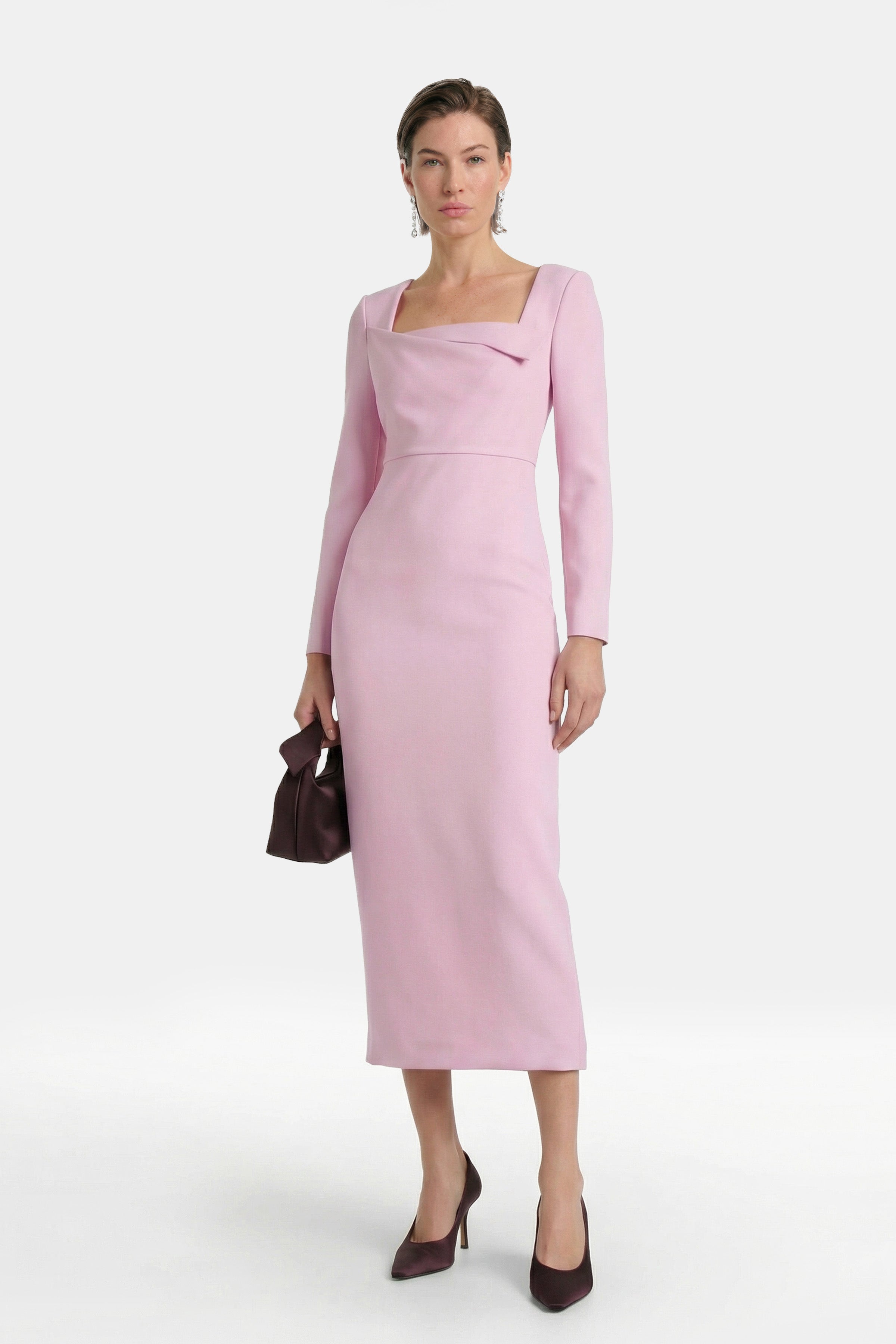 Model in pink midi dress, long sleeves, square neckline, holding a brown handbag.