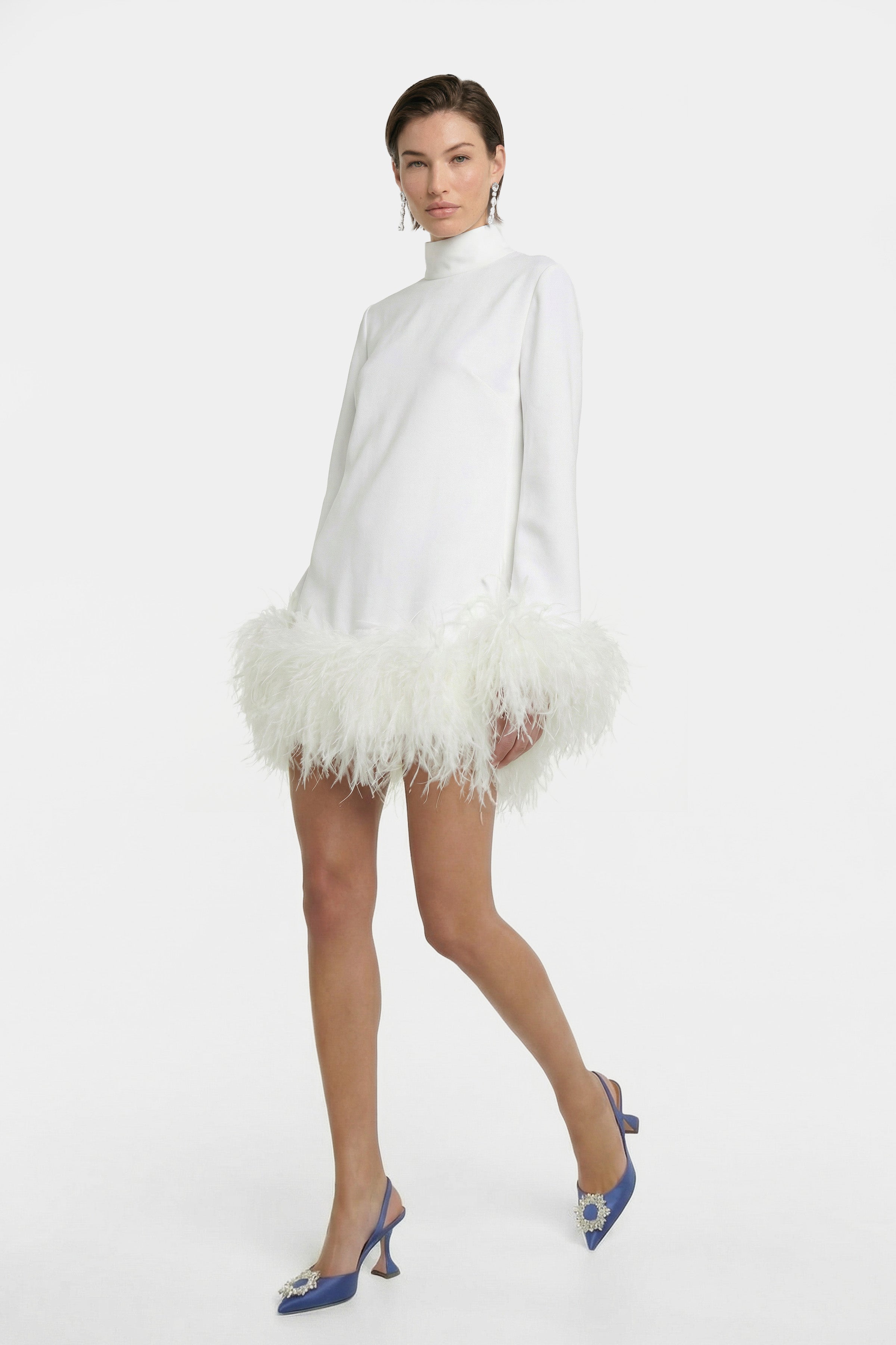 Model wearing white mini dress with feather trim, blue heels, front view.