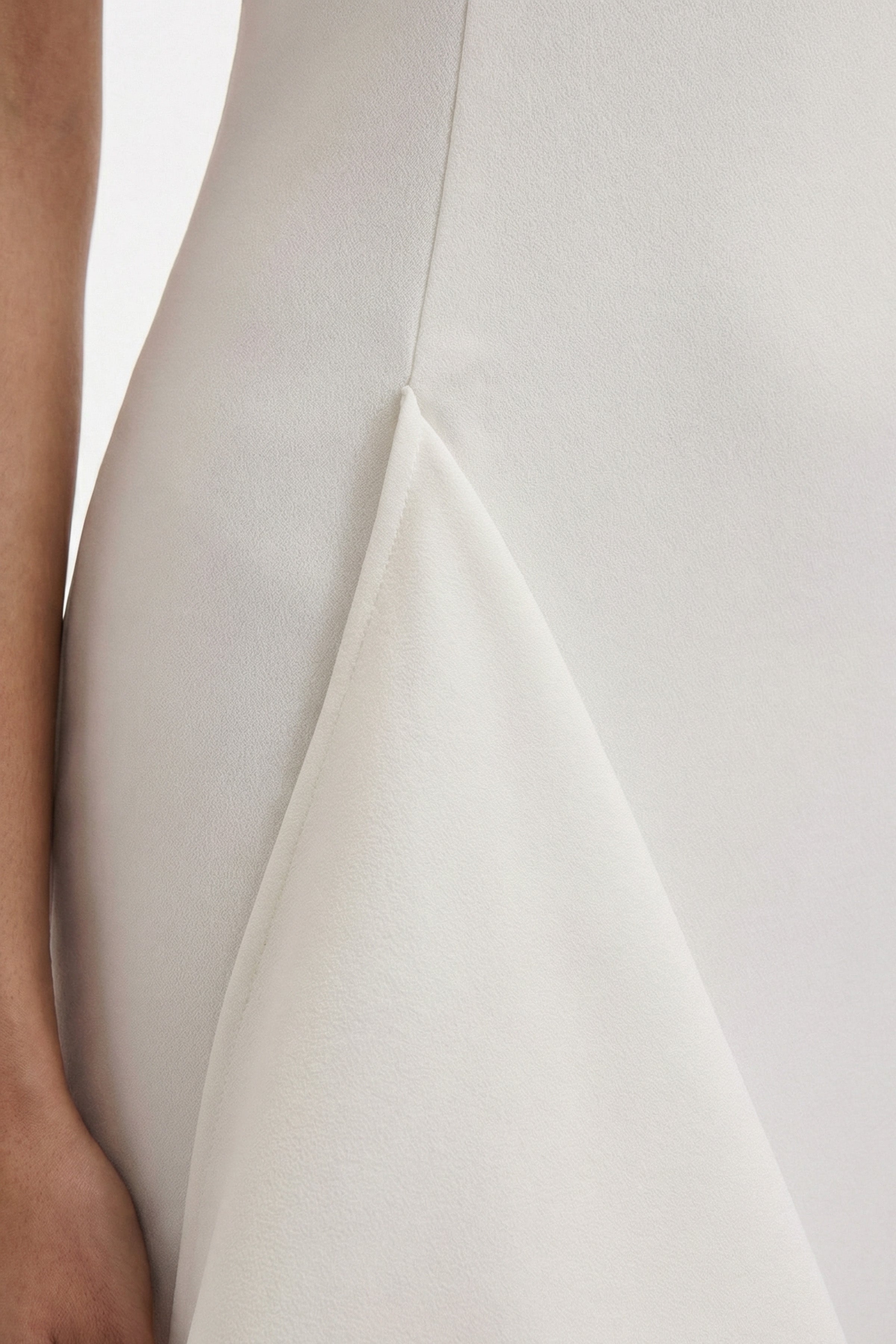 Close-up of asymmetrical white dress fabric detail, showing texture and design.