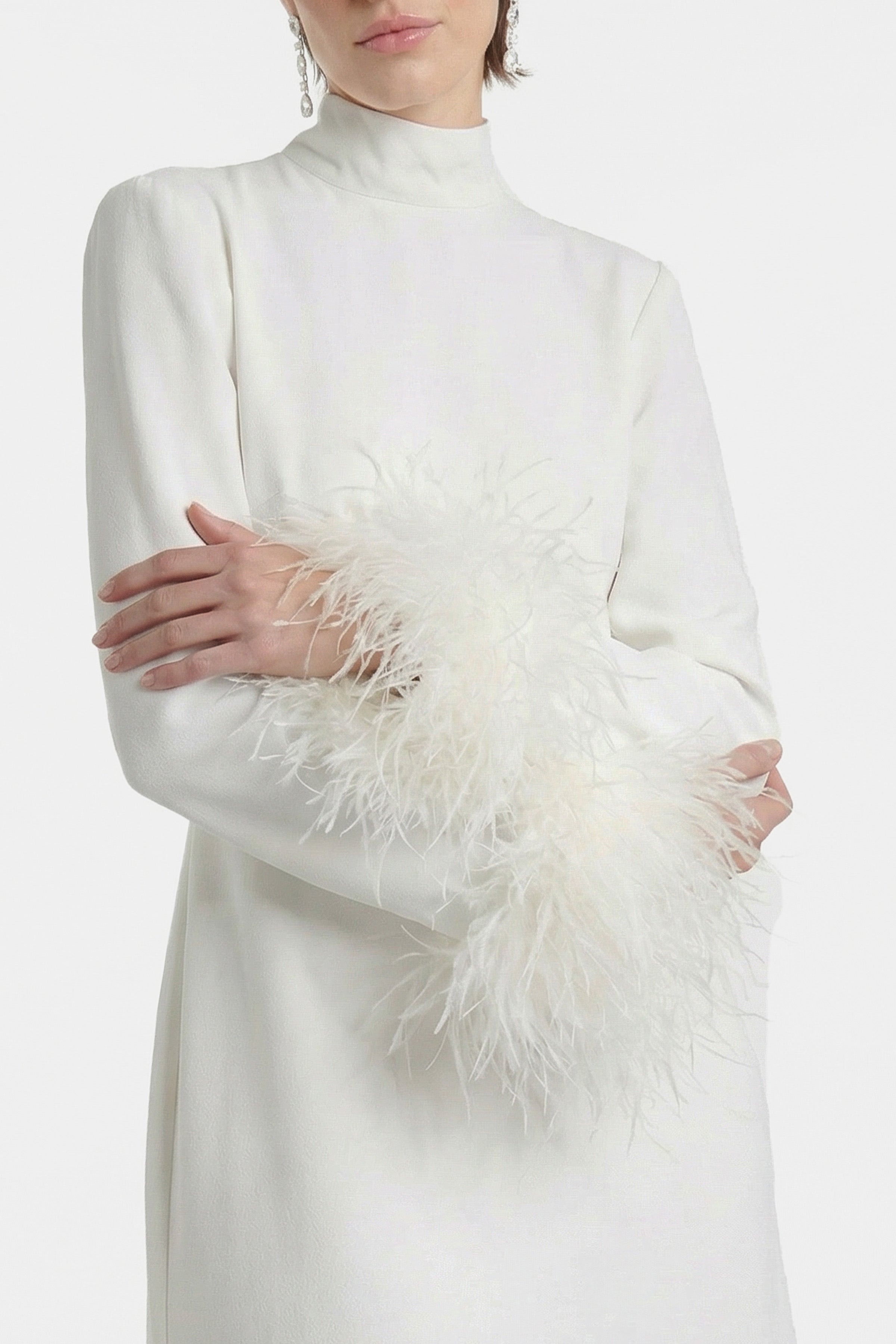Close-up of white dress with feather-trimmed sleeves, model facing forward.