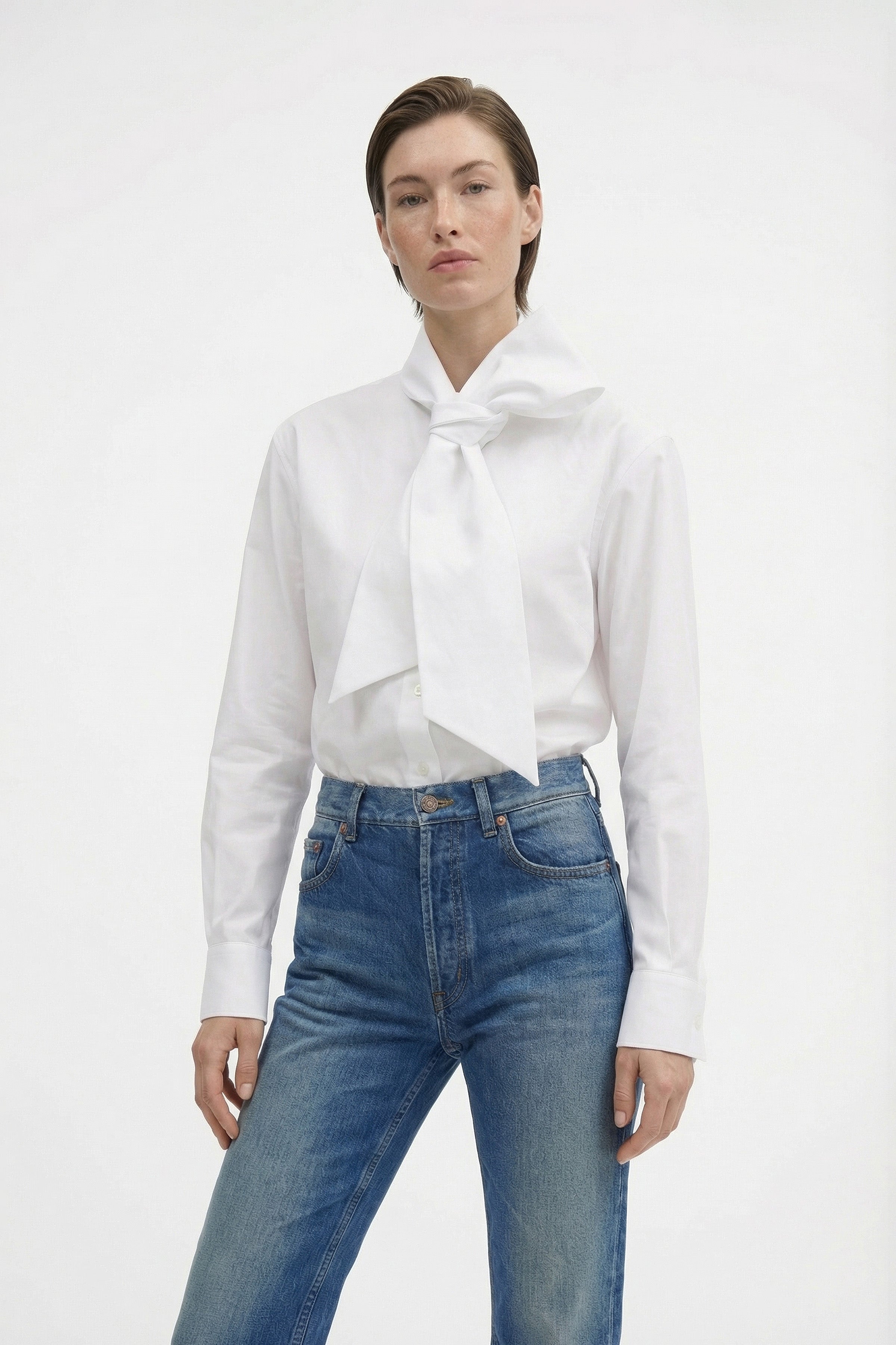 White blouse with large bow, front view, paired with high-waisted blue jeans.