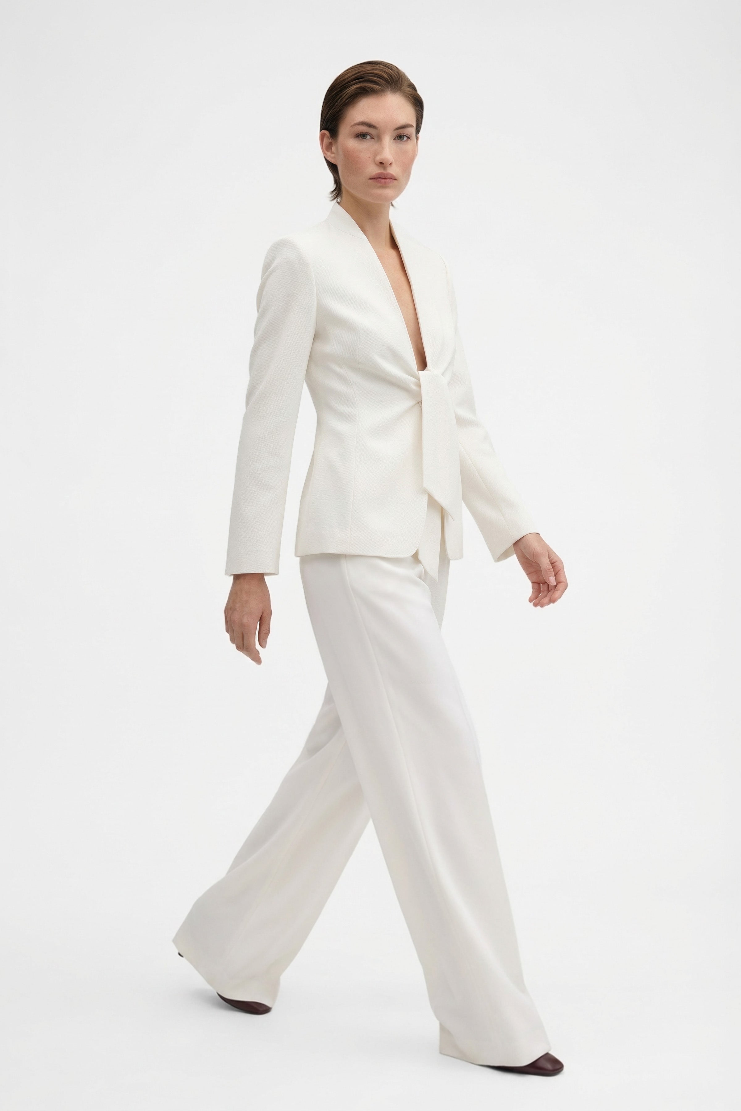 Model in ivory tie-front suit, front view, walking, elegant look, stylish ensemble.