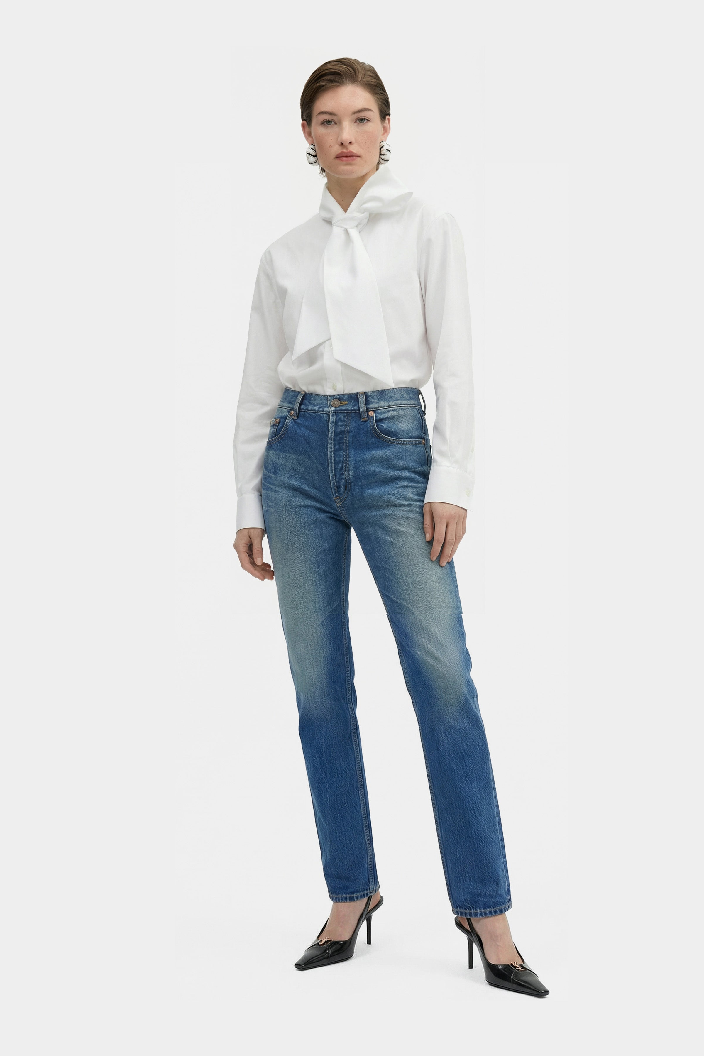 Model wearing elegant white bow blouse with jeans, front view.