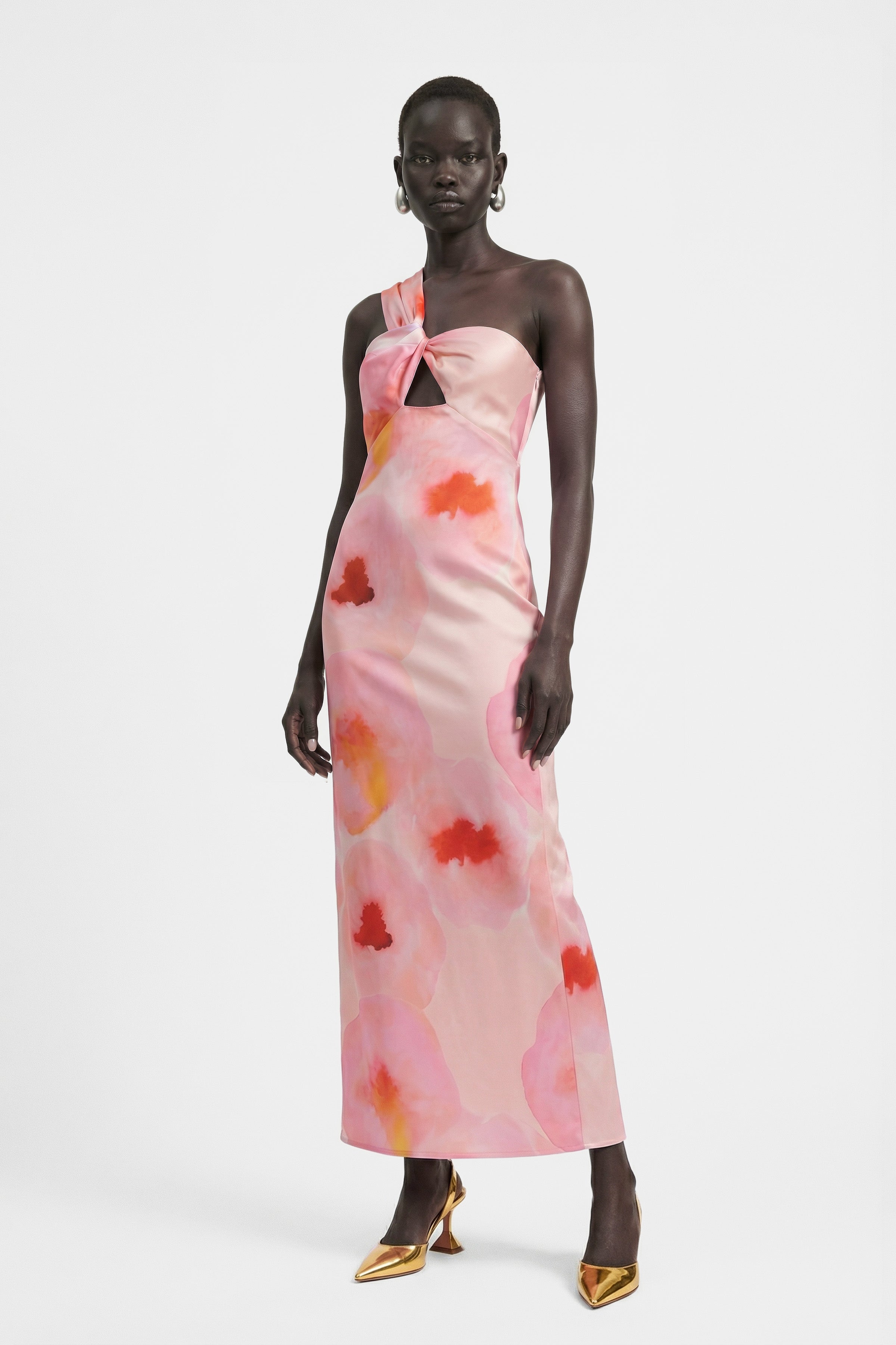 Model in watercolor one-shoulder dress, pink-orange print, standing front view.