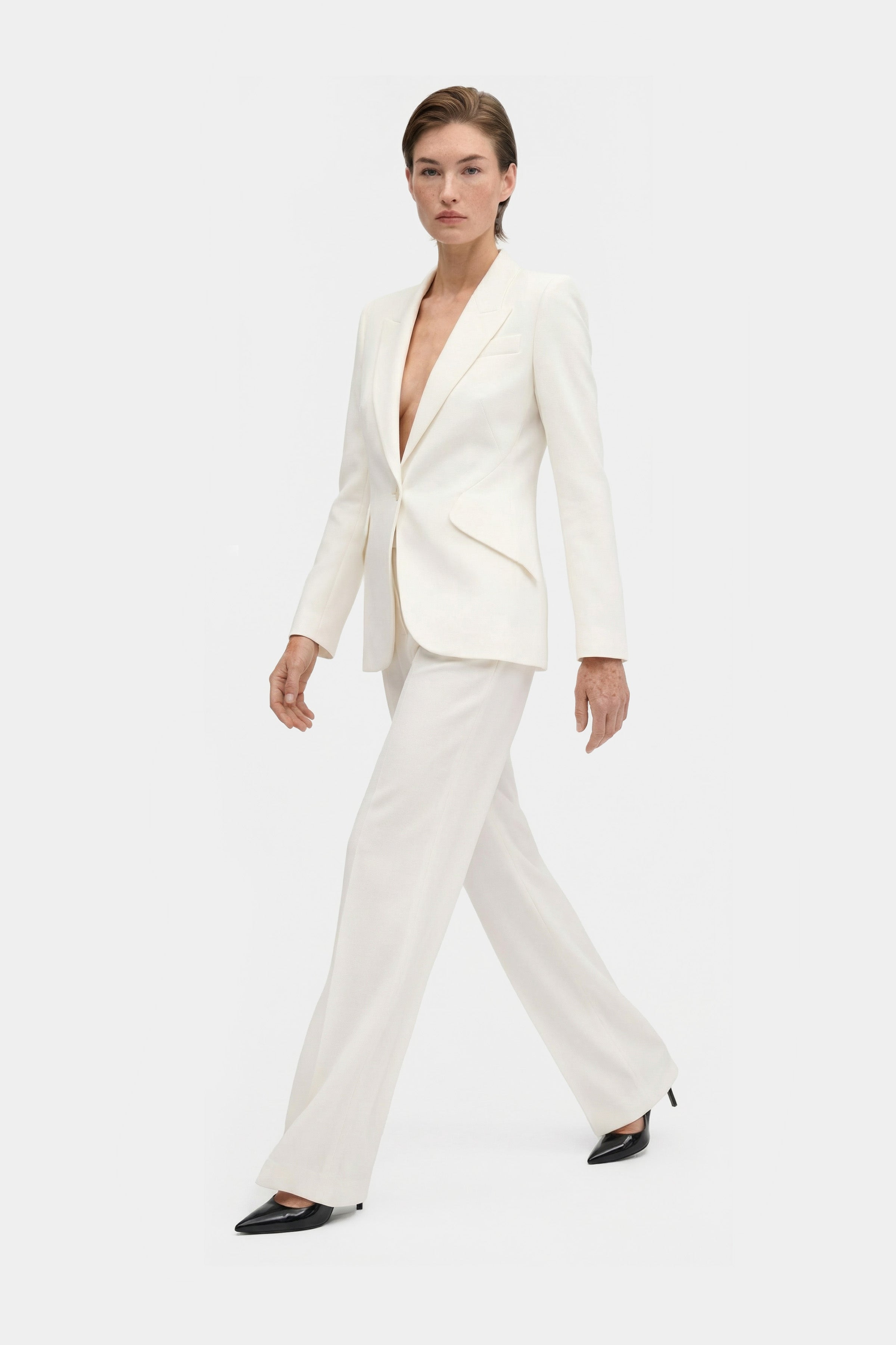 Model walking in an ivory tailored blazer, front view, paired with matching pants.