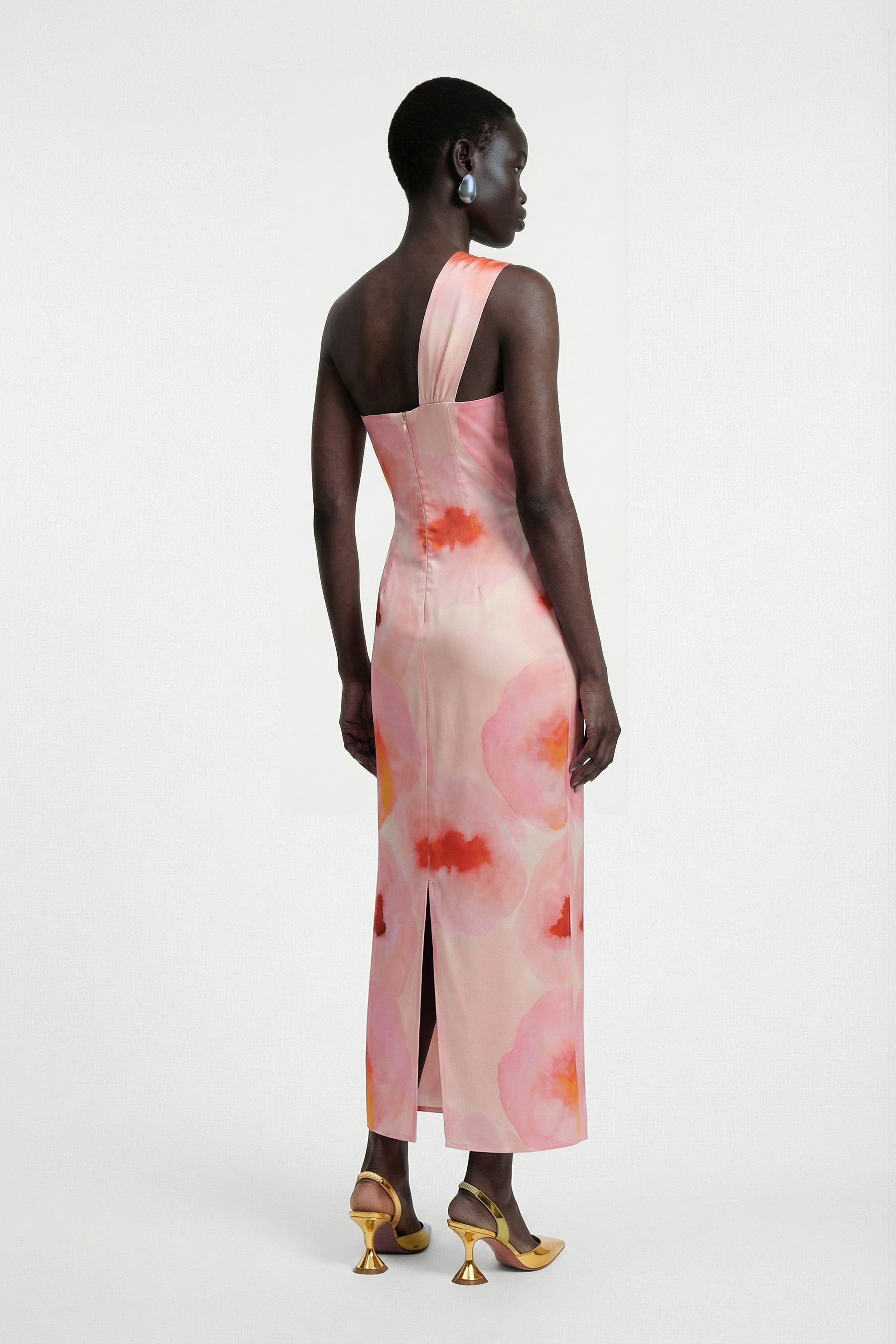 Back view of model in watercolor one-shoulder dress, slit detail, colorful heels.