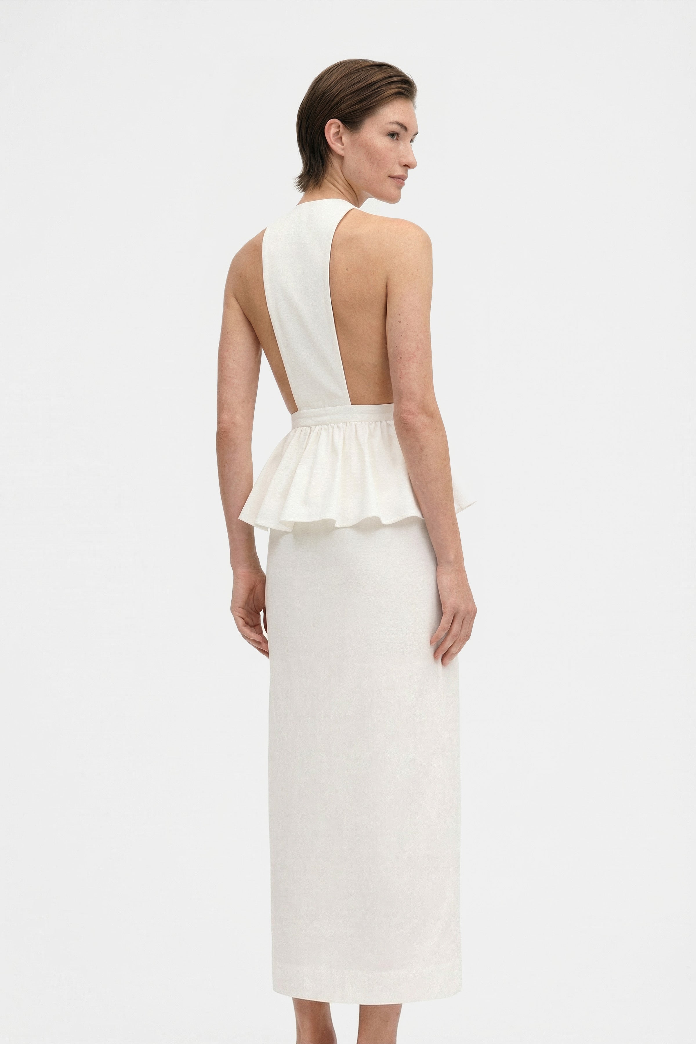 Back view of model wearing a white halter peplum dress with open back.