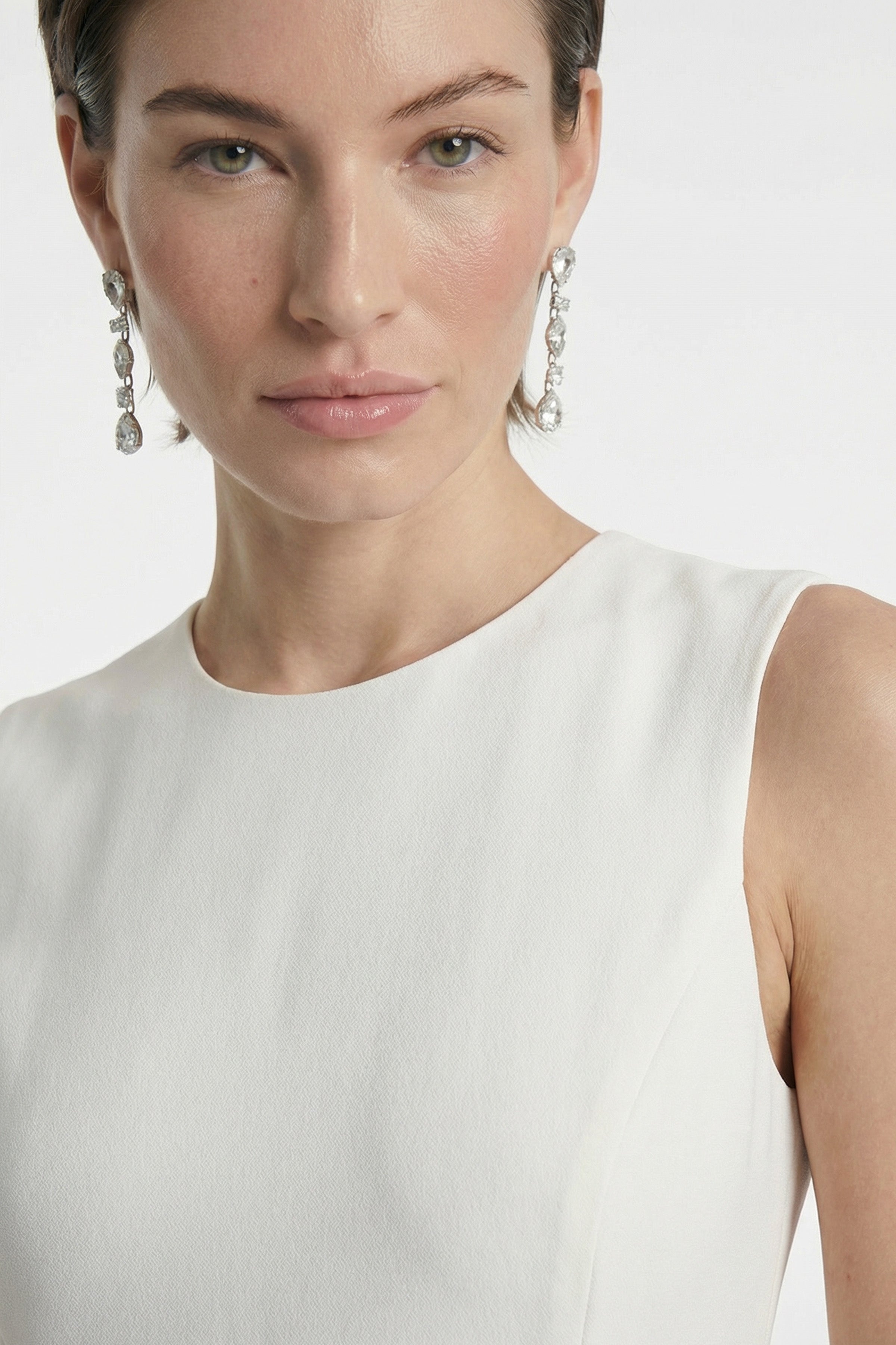 Close-up of the asymmetrical white dress's textured fabric, worn with elegant drop earrings.