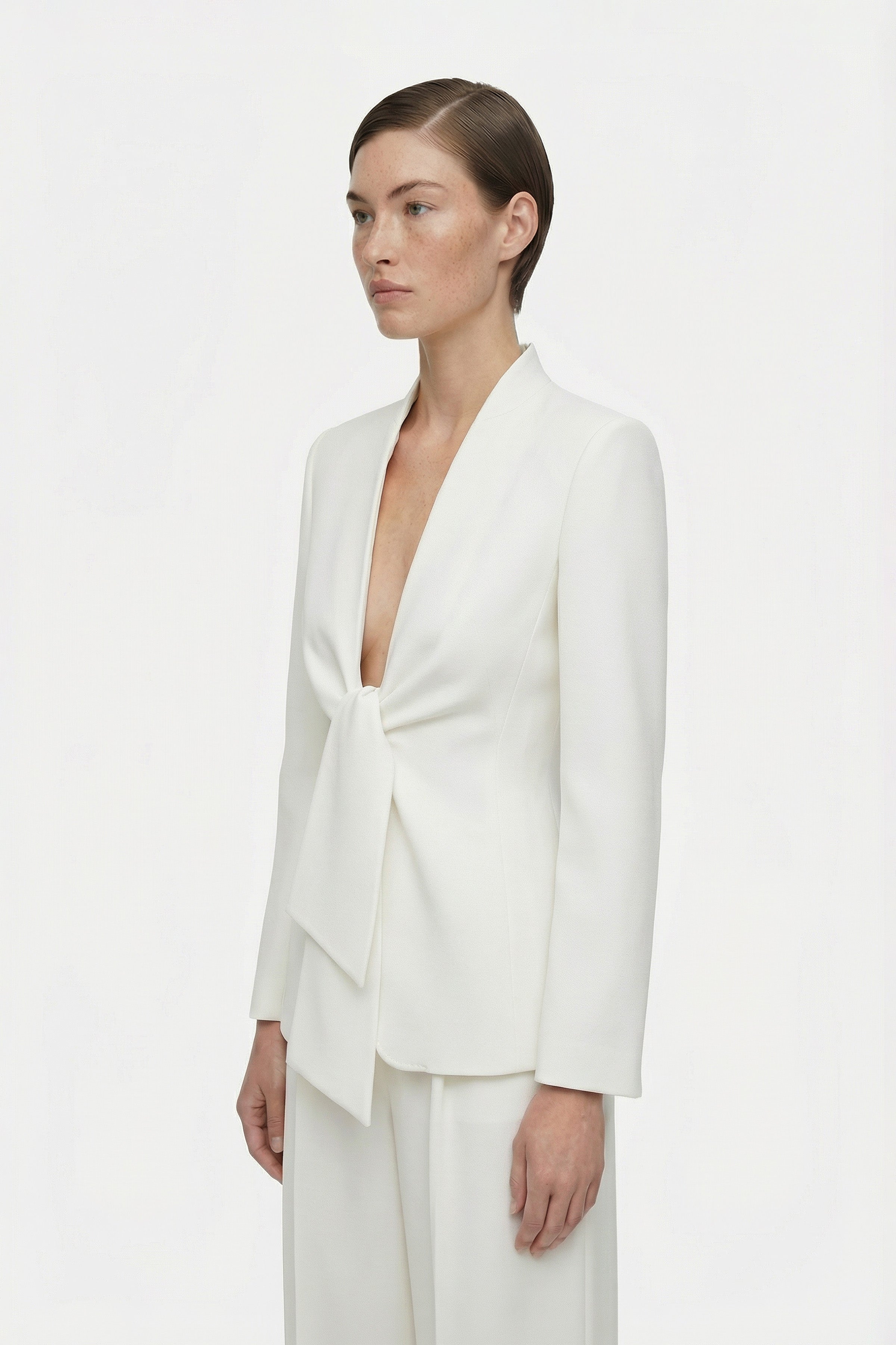Model wearing ivory suit with tie-front detail, side view.