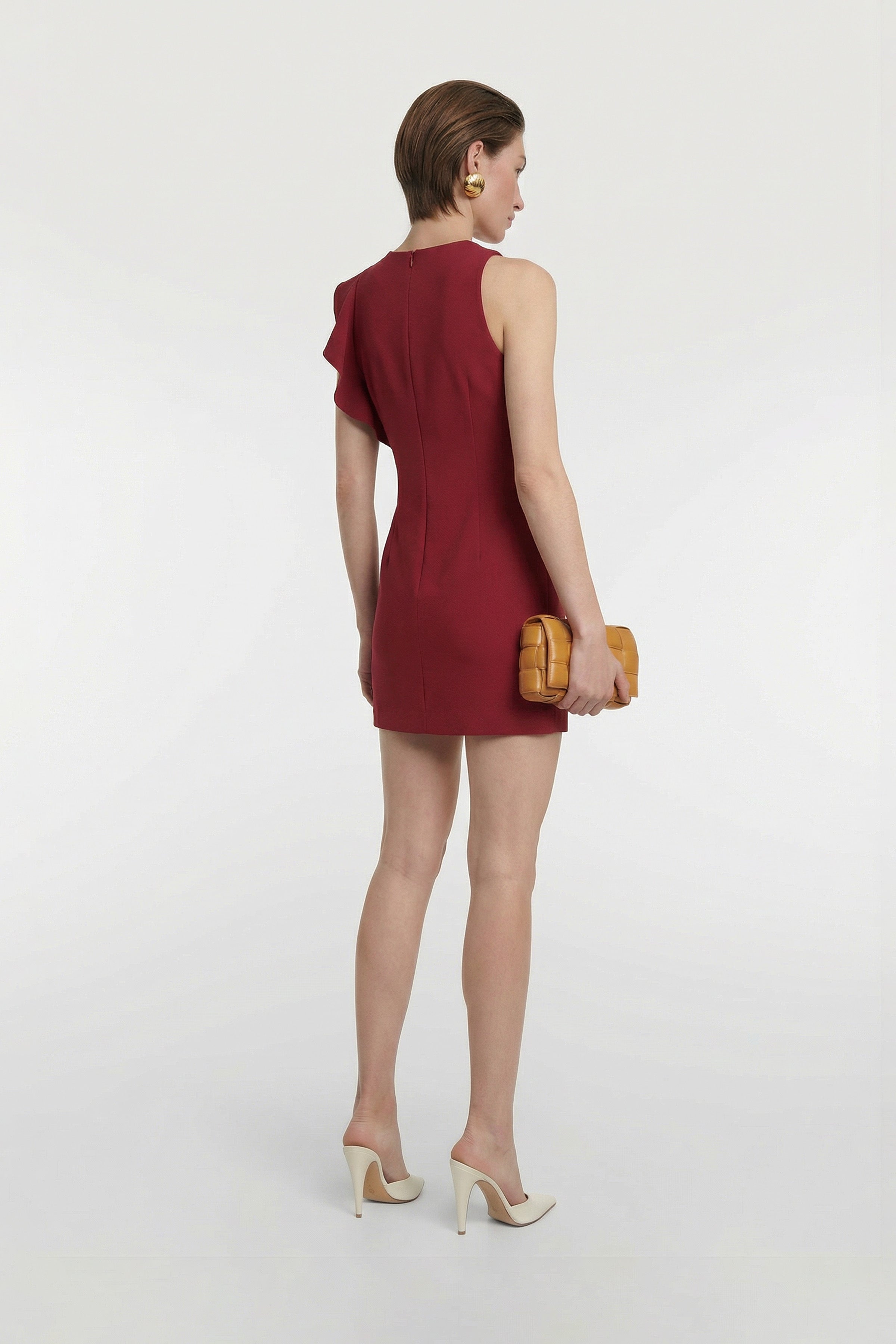 Back view of model wearing ruffled scarlet mini dress, with beige heels and clutch.