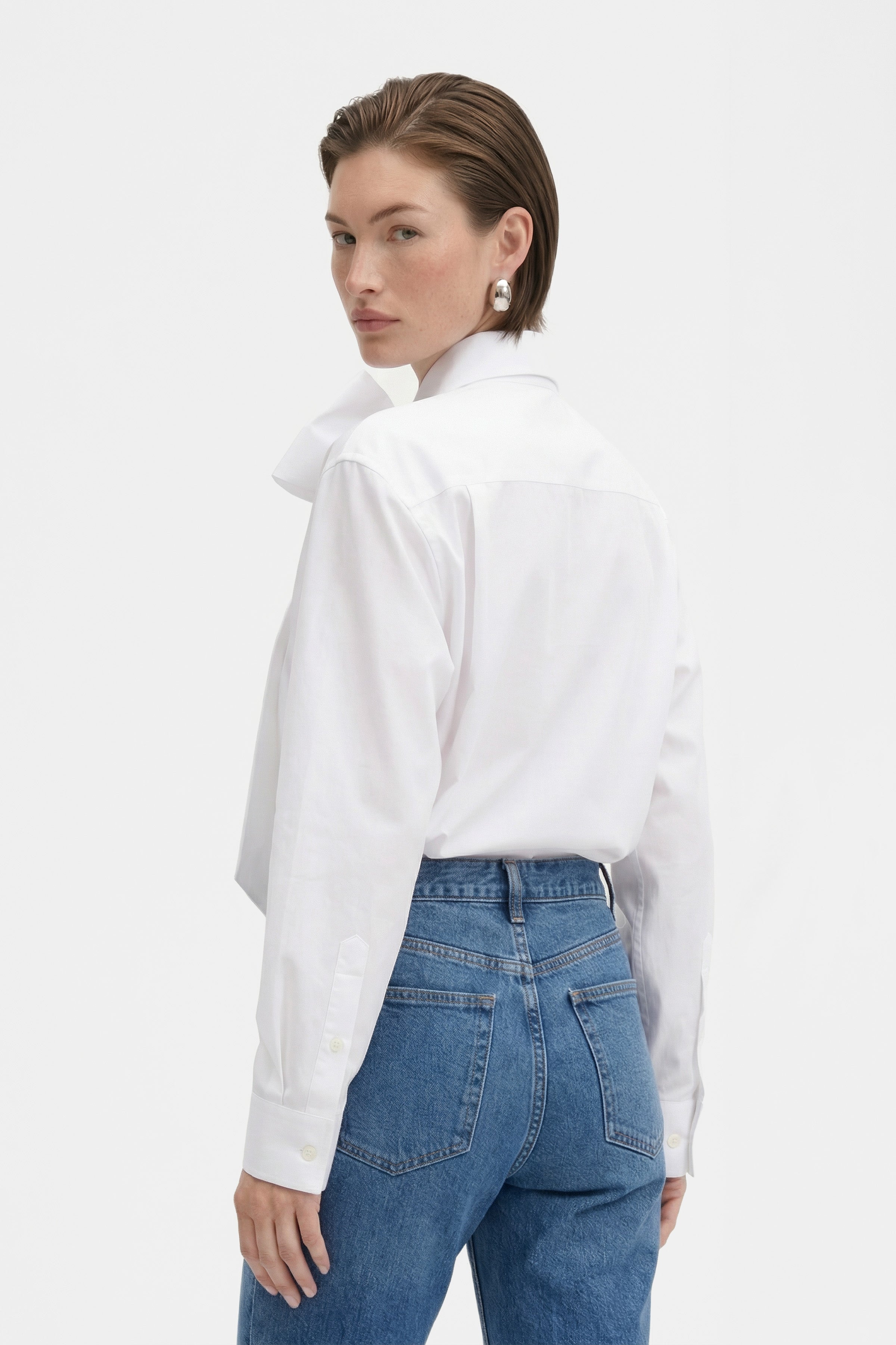 Back view of model in white bow blouse with jeans, looking over shoulder.