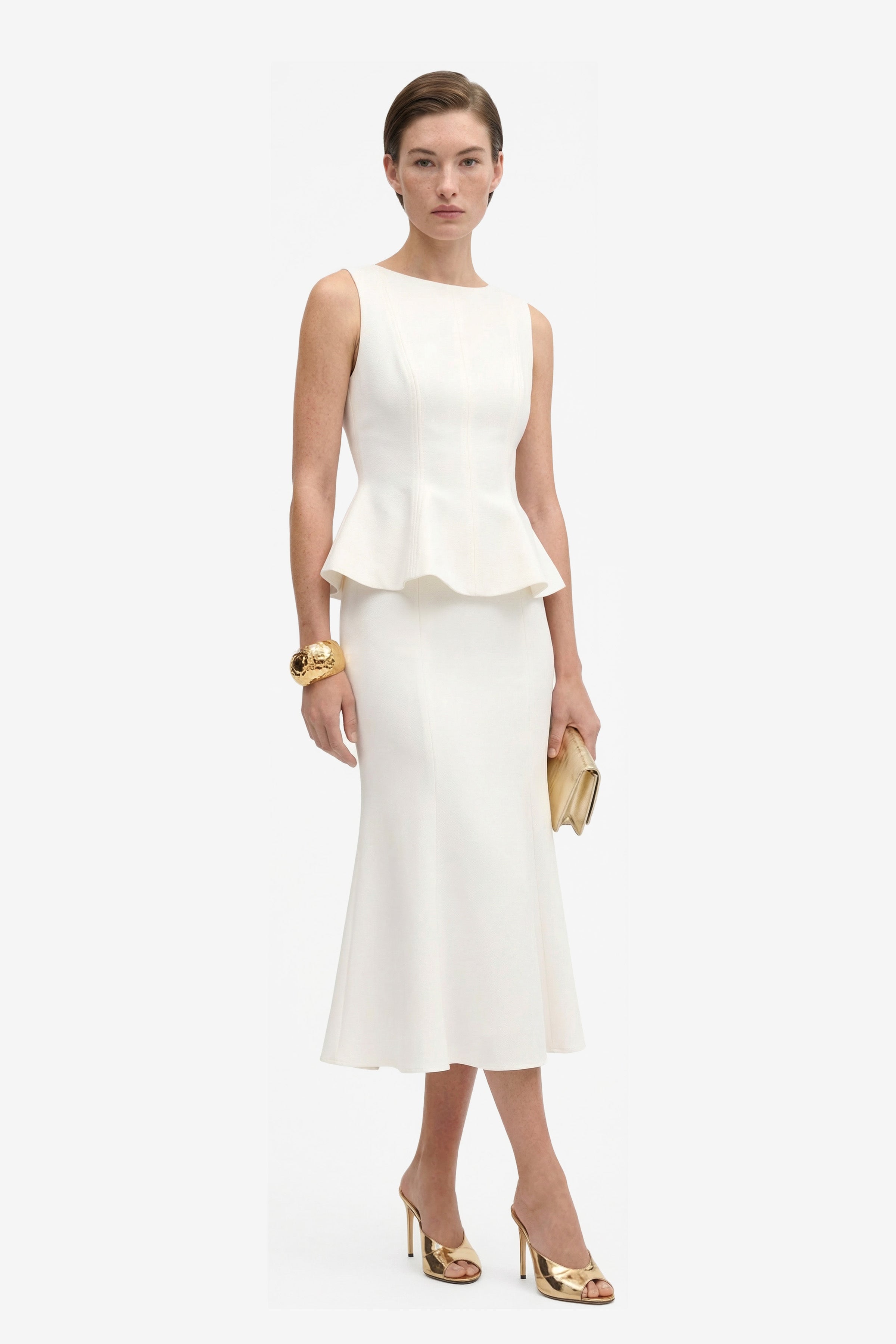 Model wearing Ivory Elegance Midi skirt, peplum detail, holding clutch, gold heels.