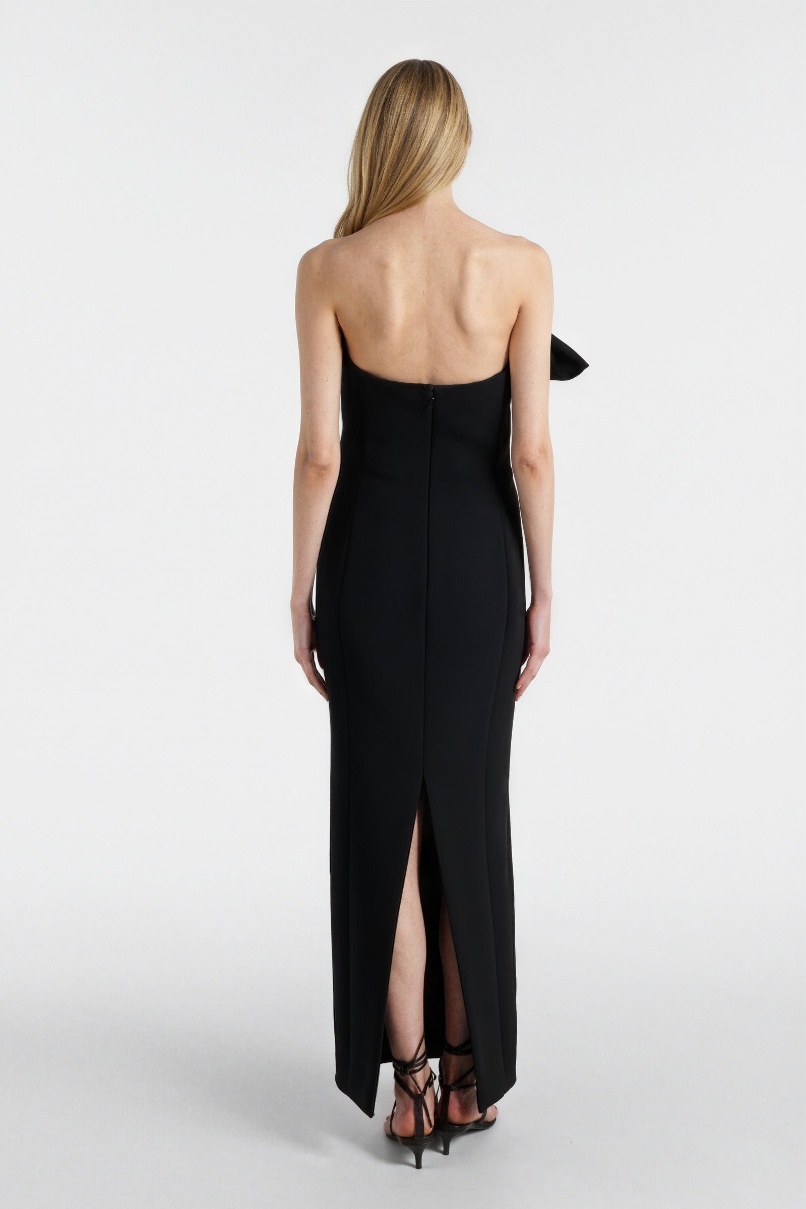 Back view of a black one-shoulder evening gown with slit hem and fitted silhouette.