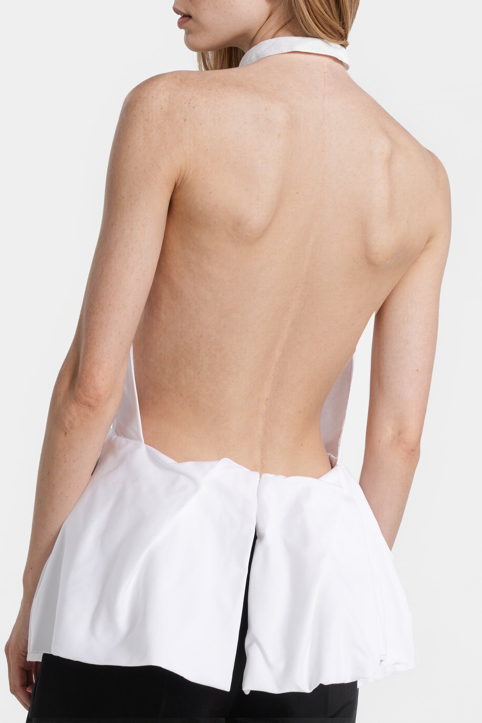 Close-up side view of a woman wearing a sculptural white halter top with a high neckline.