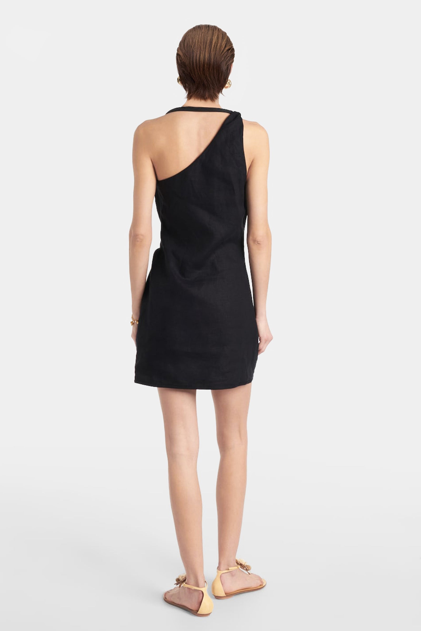 Back view of the black linen mini dress on a model, showing the asymmetric strap detail and the tailored fit.
