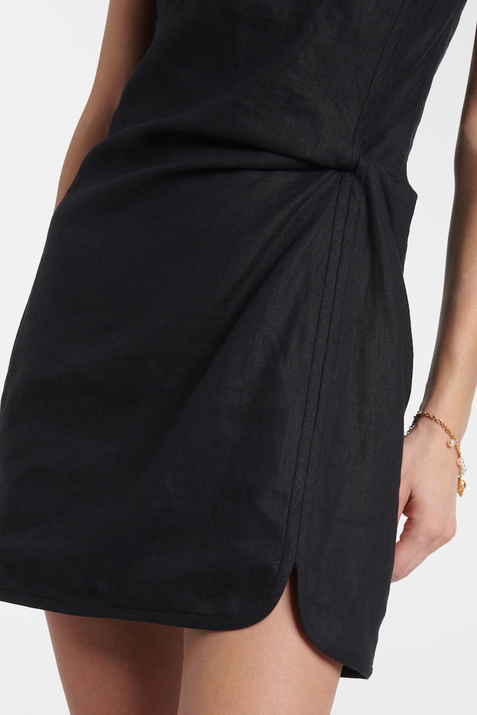 Detailed shot of the decorative side knot and the subtle draping on the skirt of the black linen mini dress.