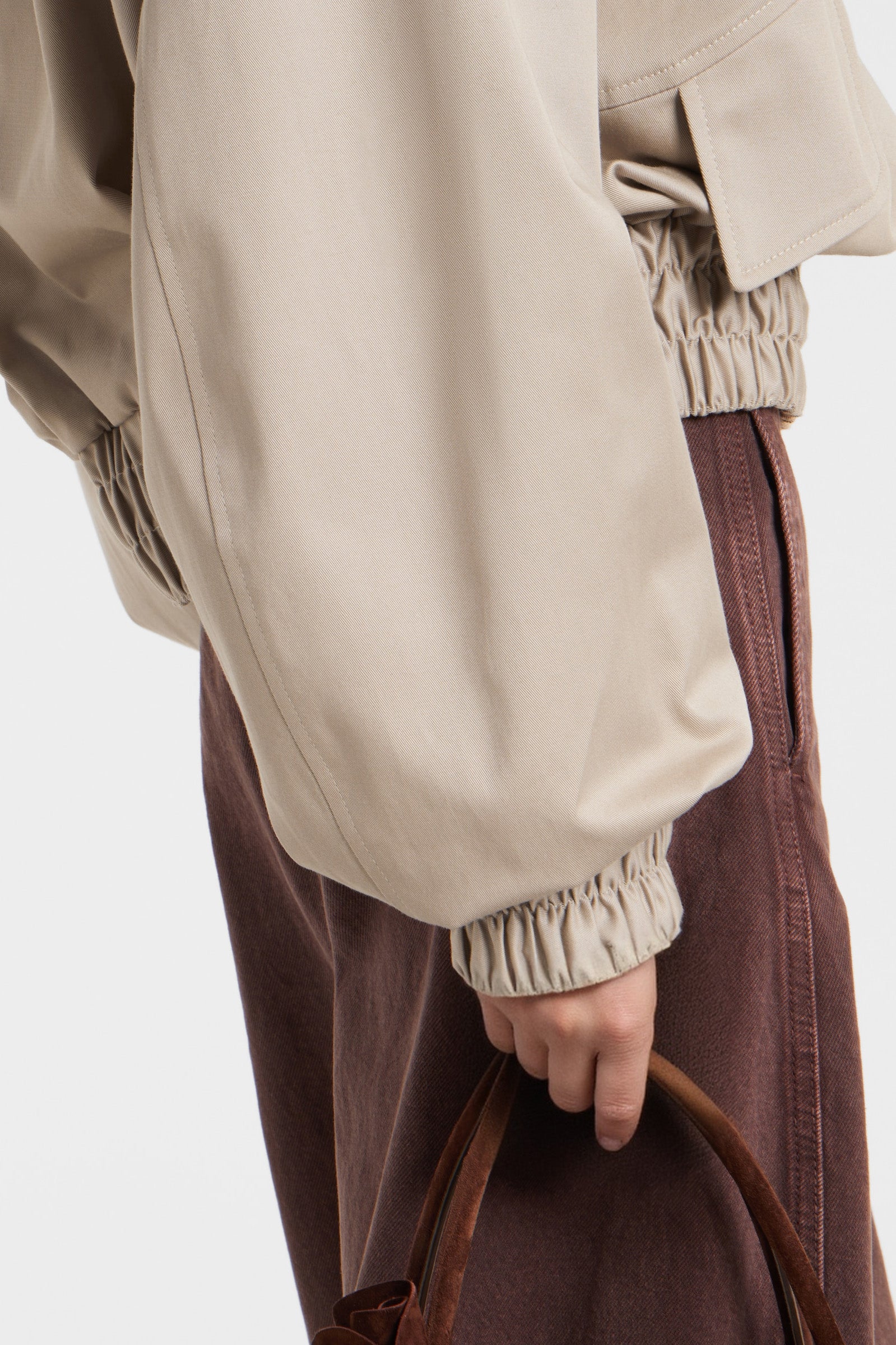 Close-up of beige bomber jacket with flap pockets and zipper