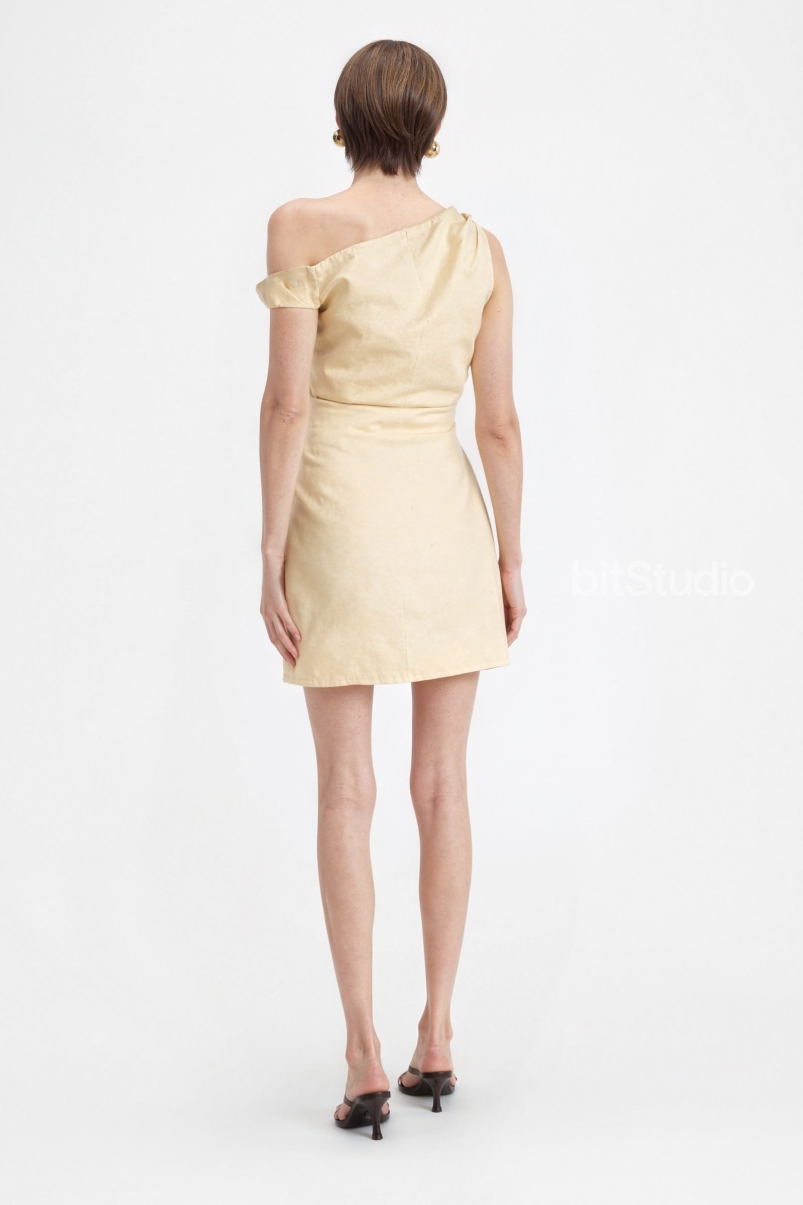 Back view of the yellow linen mini dress on a model, showing the asymmetric neckline and the simple, clean lines of the skirt.