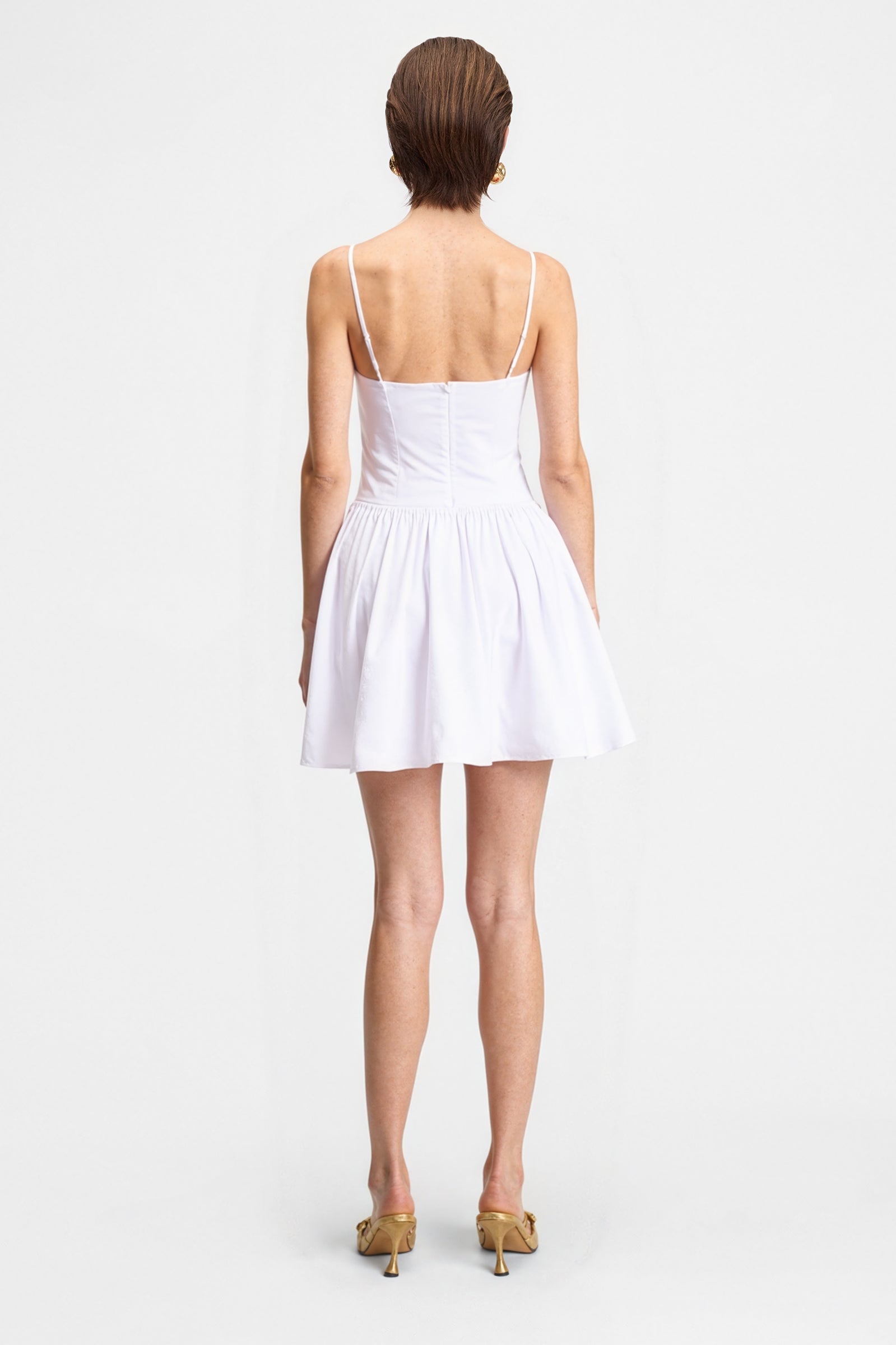 Back view of the white poplin cotton mini dress on a model, showing the delicate spaghetti straps and the gathered A-line skirt.