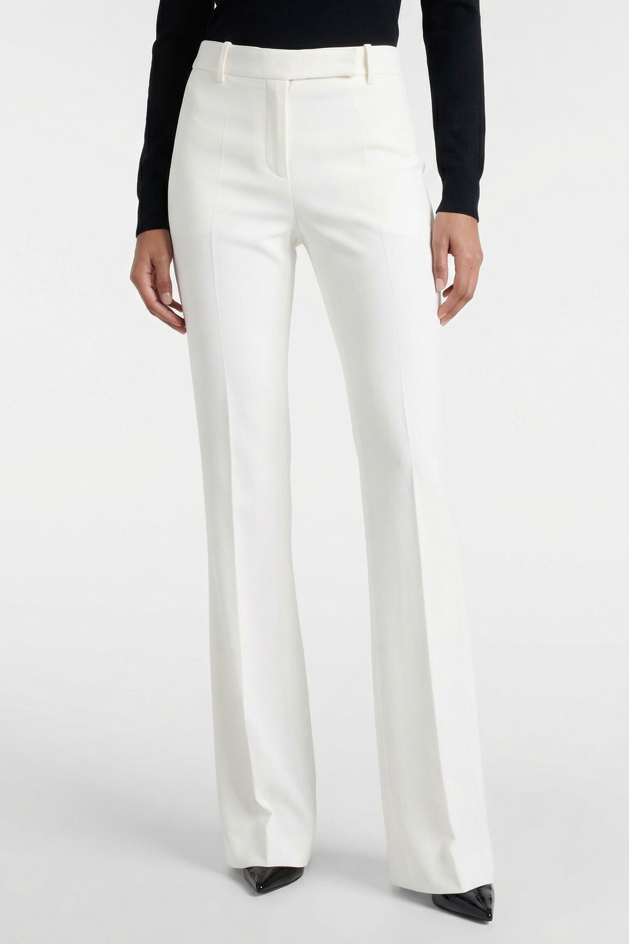 Model wearing ivory tailored flare pants, front view, with black pointed shoes.