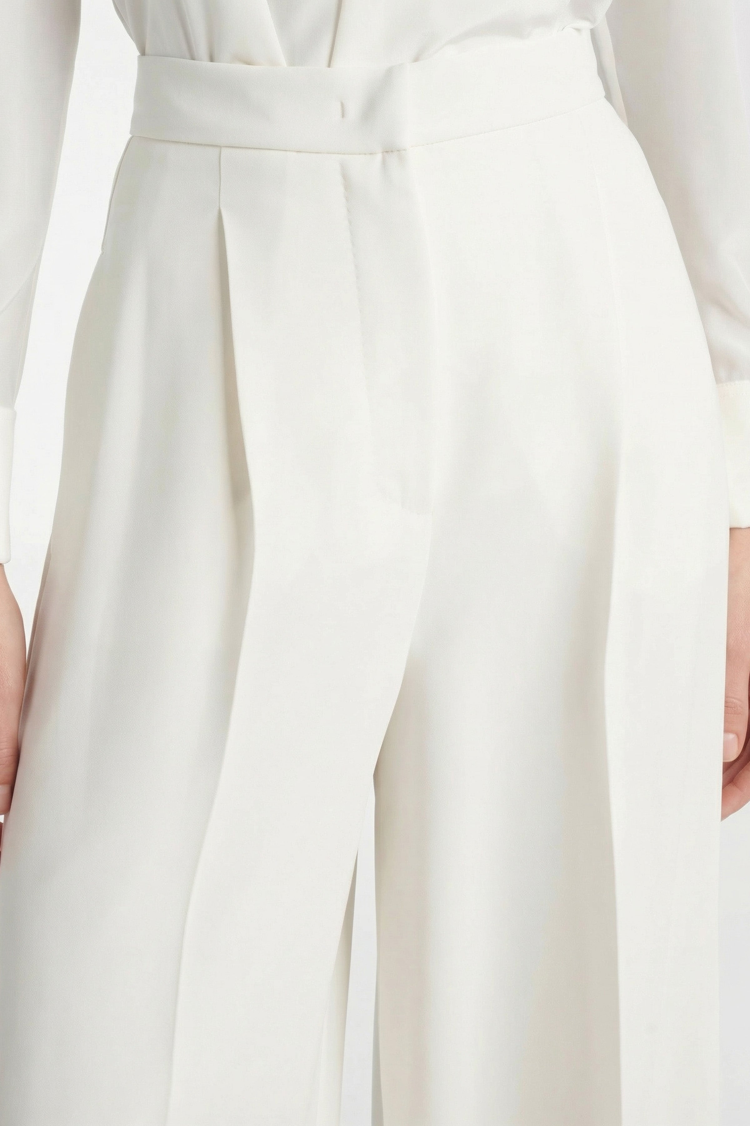 Close-up of ivory wide-leg trousers detailing waistband and pleats.