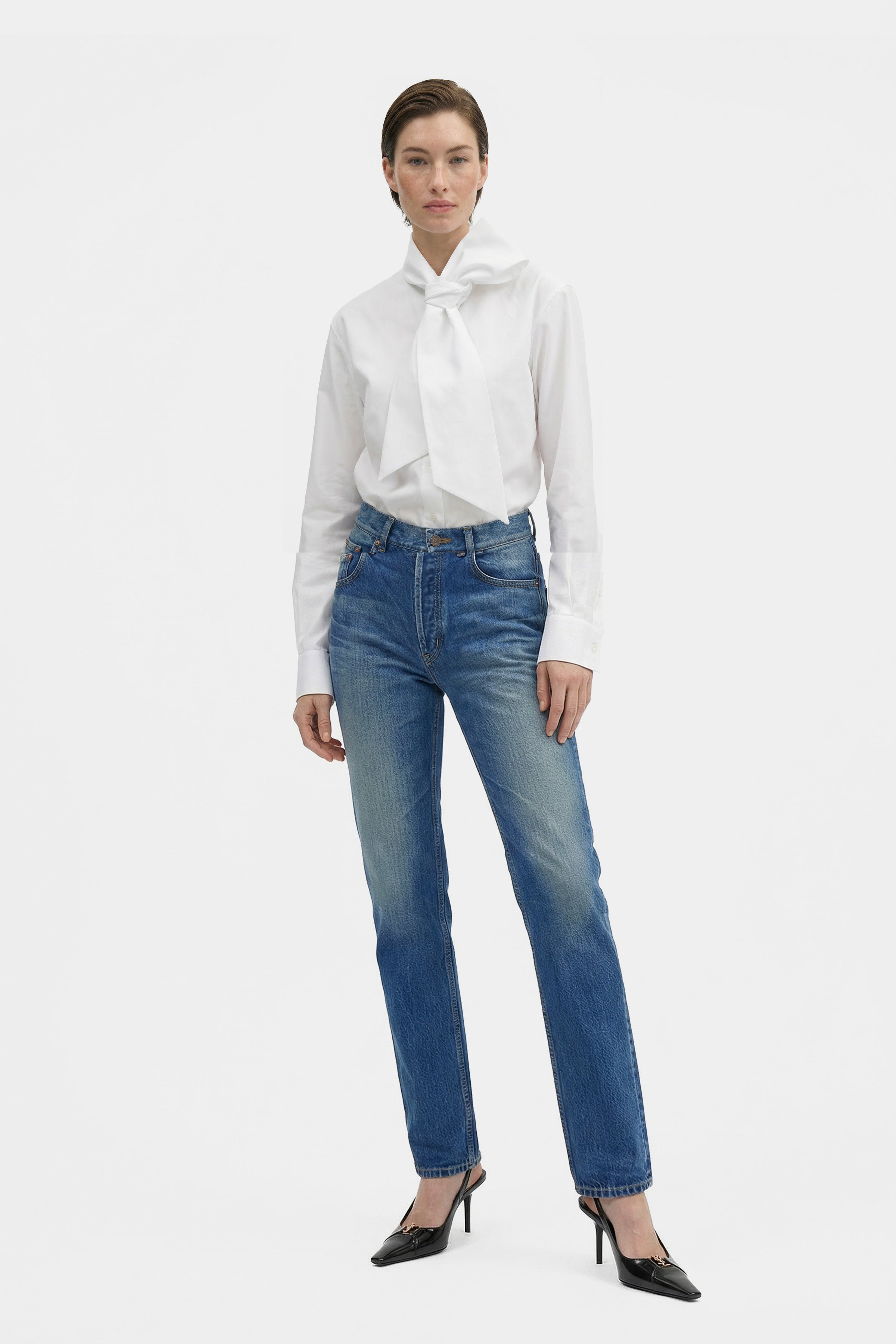 Model wearing elegant white bow blouse with jeans, front view.
