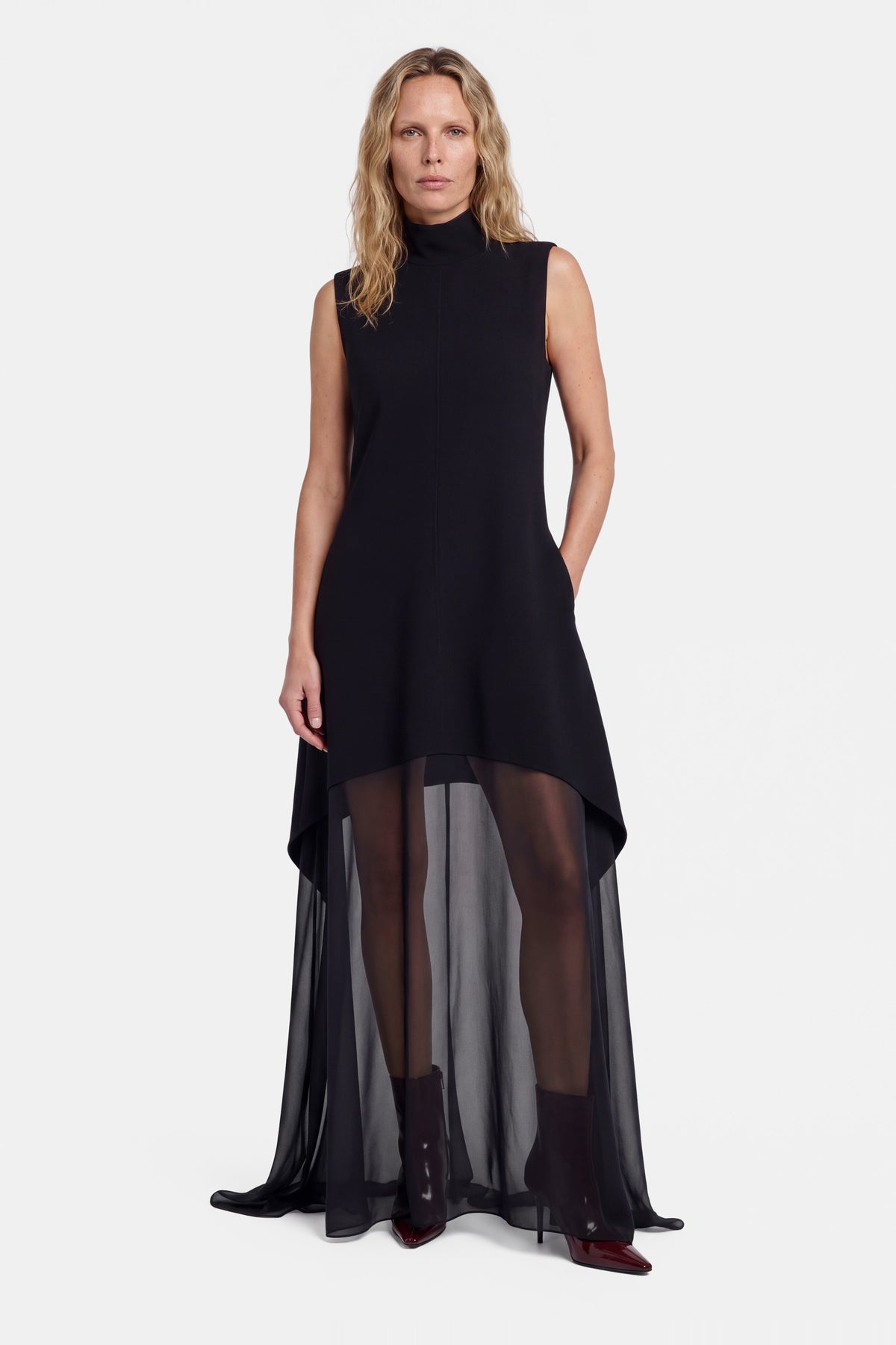 Black sheer overlay dress with high-low hem, sleeveless, model wearing burgundy ankle boots.