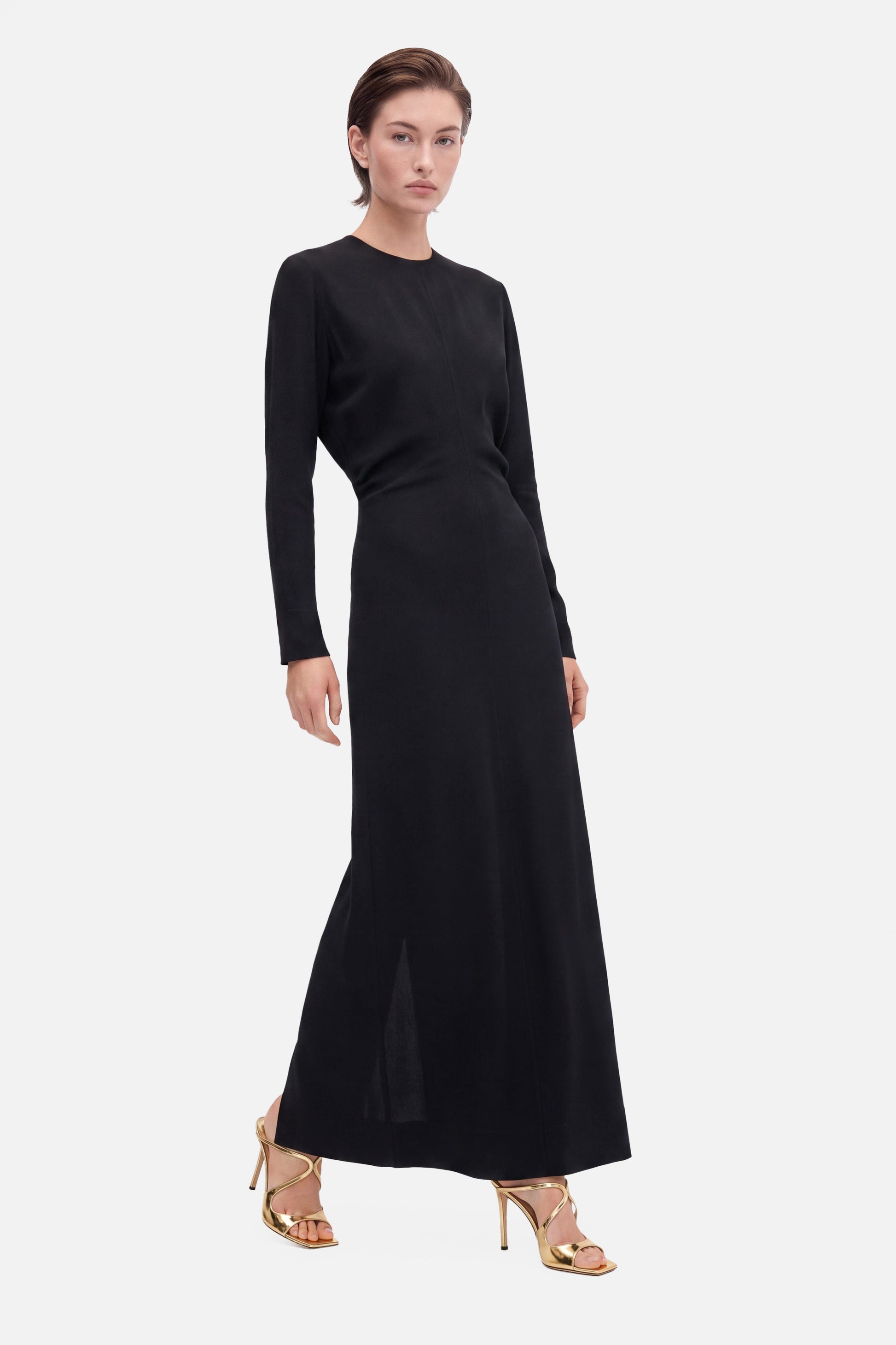 Model wearing black long sleeve maxi dress, front view, gold heels, minimalistic style.