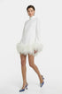 Model wearing white mini dress with feather trim, blue heels, front view.
