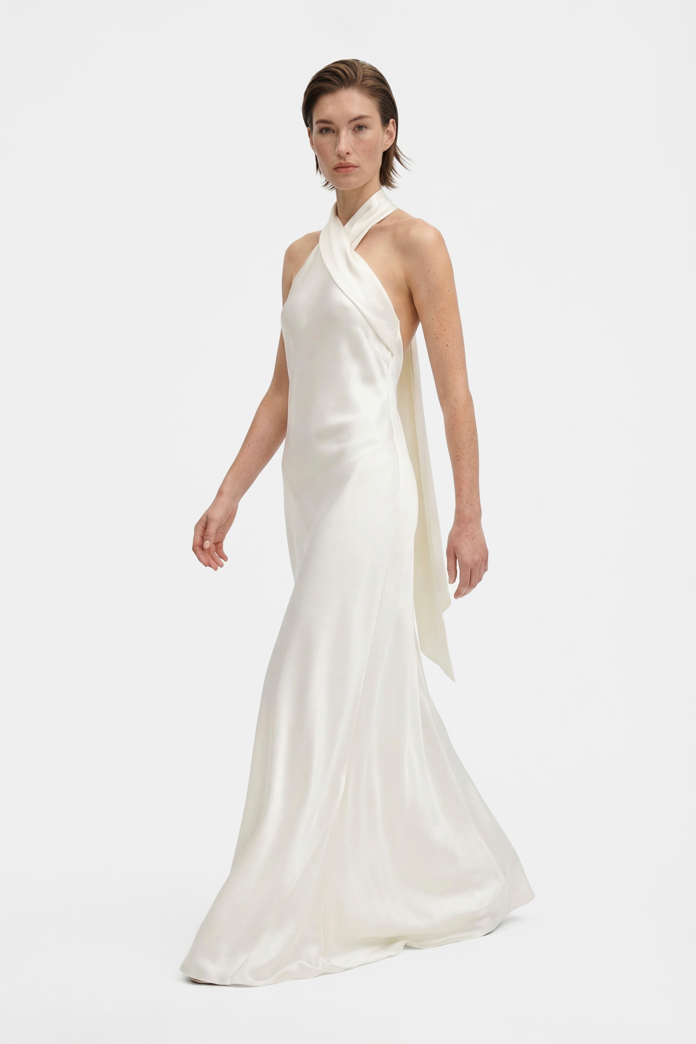 Model in silk halter gown, side view in motion, smooth and elegant drape.
