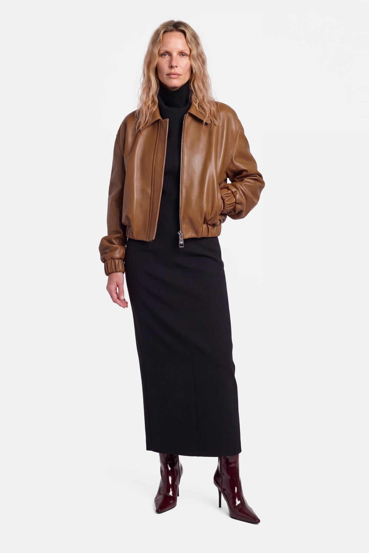Model wearing cognac leather bomber jacket, front view, paired with black dress.