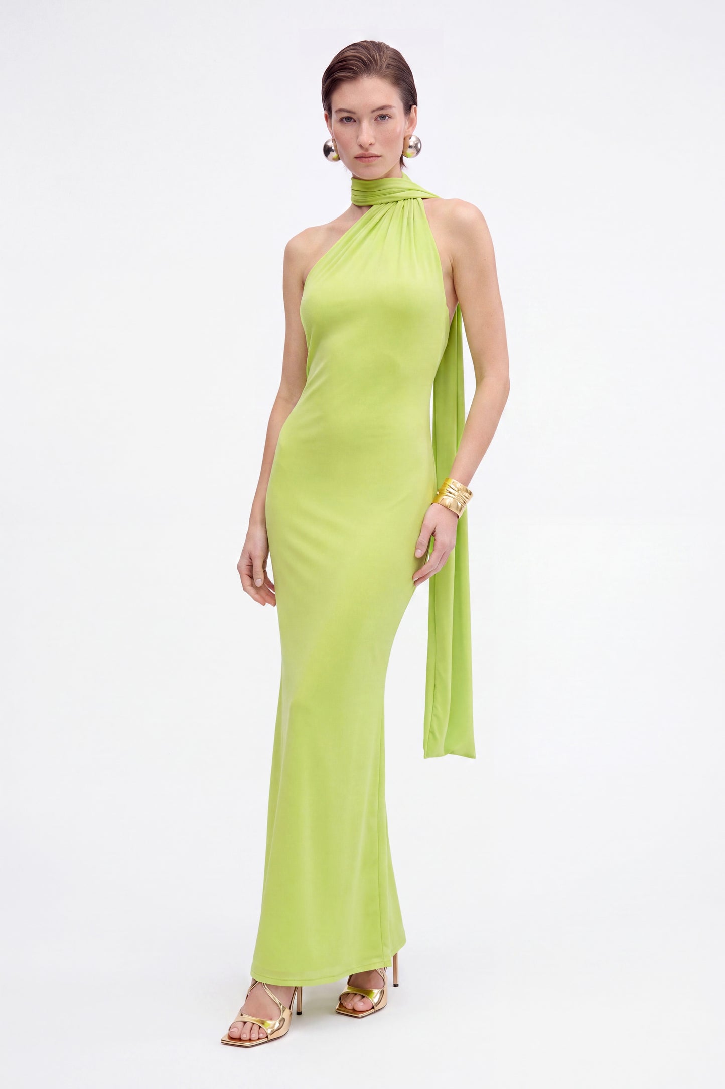Model in lime asymmetric halter dress, front view, gold accessories, white background.