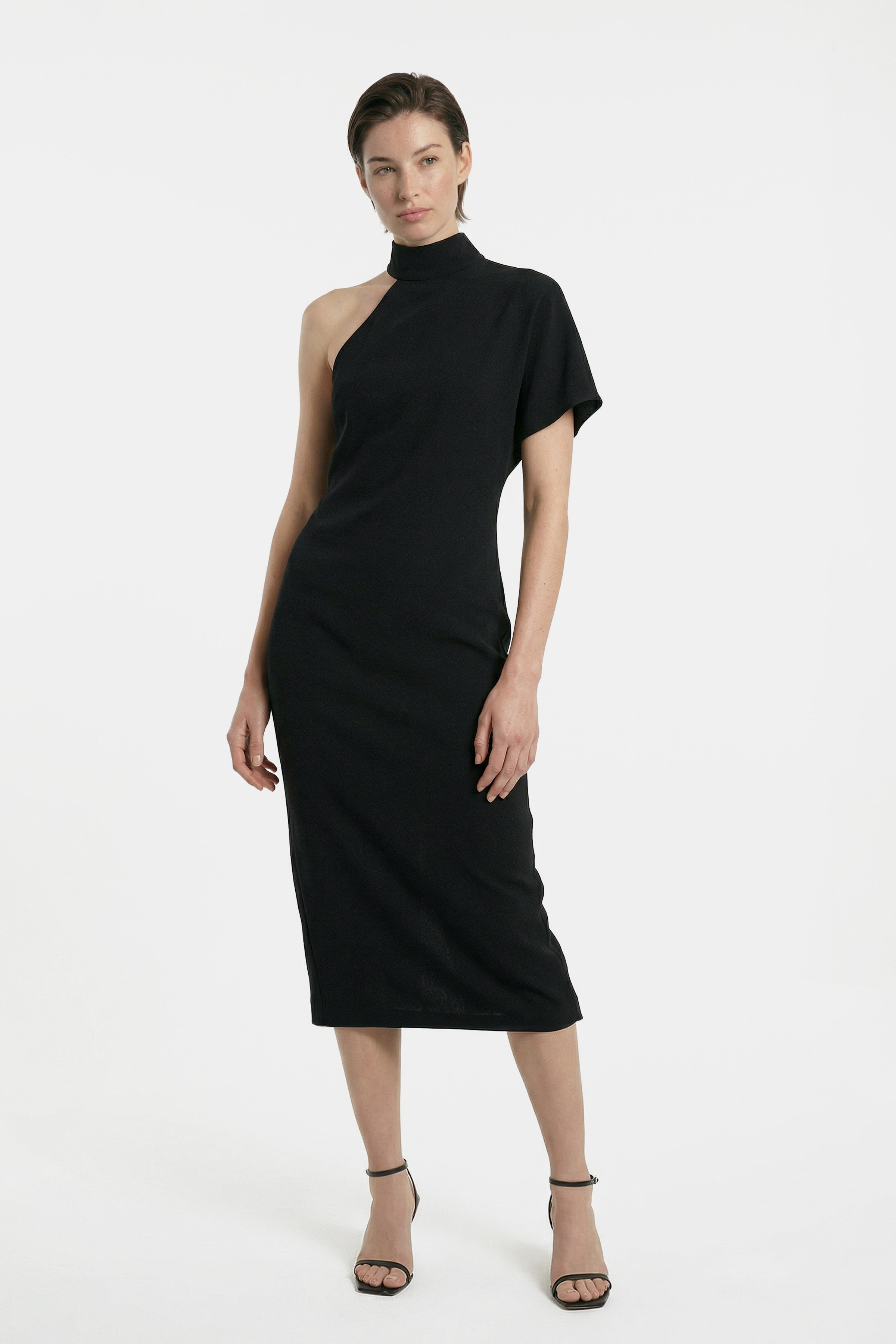 Front view of asymmetrical black midi dress, one shoulder design, on model standing.