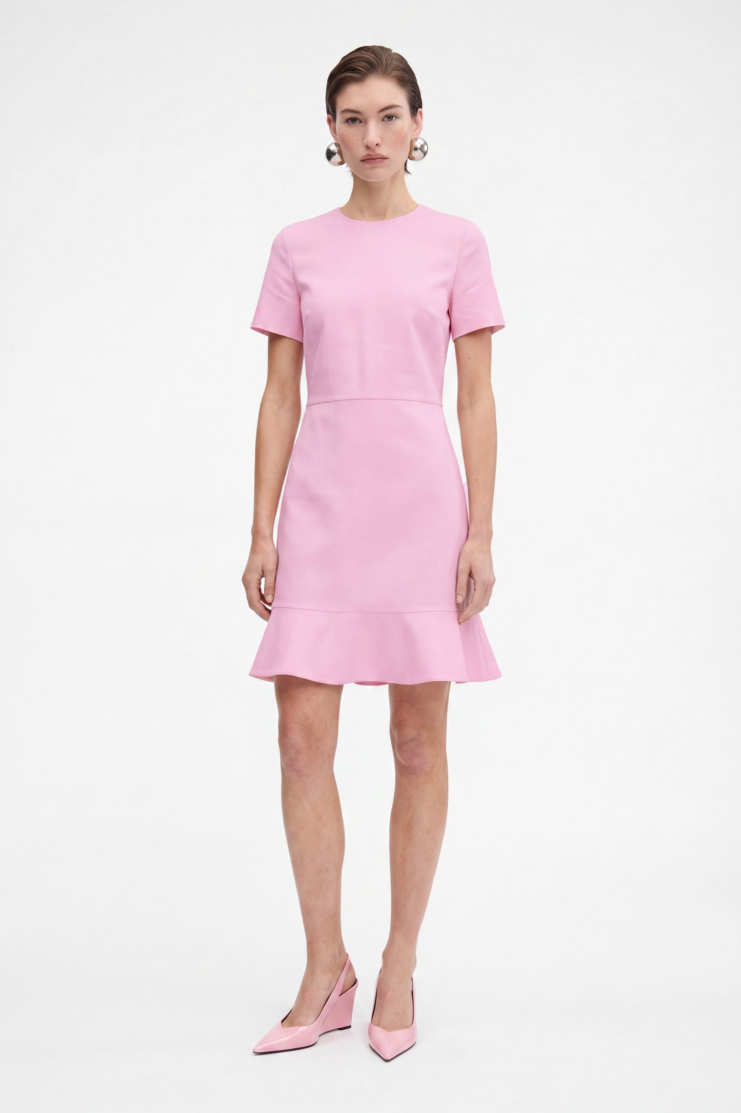 Model in pink flounce hem dress, front view, standing, wearing matching pink heels.
