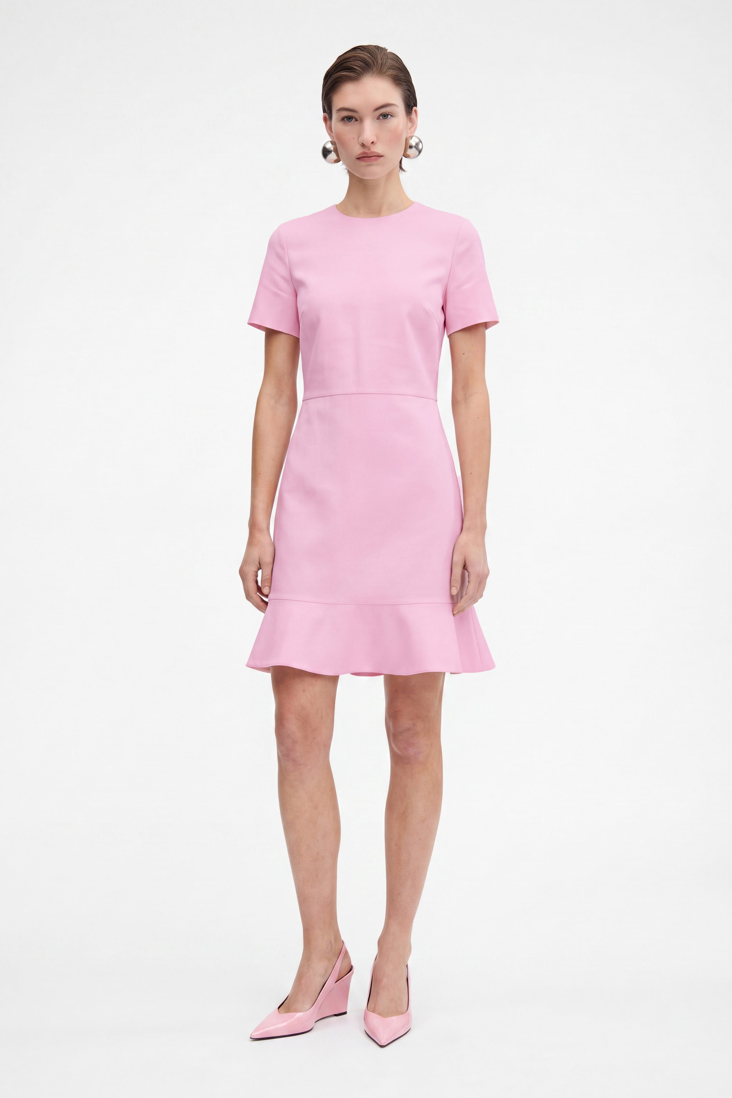 Model in pink flounce hem dress, front view, standing, wearing matching pink heels.