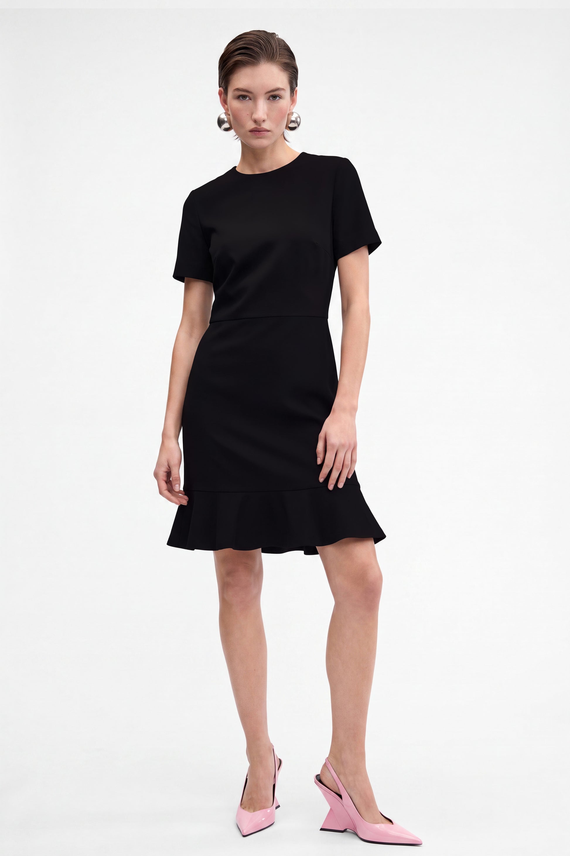 Front view of black ruffle hem dress on model with pink heels.