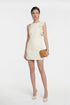 Model wearing a ruffle shoulder cream dress, holding a tan clutch, frontal view.