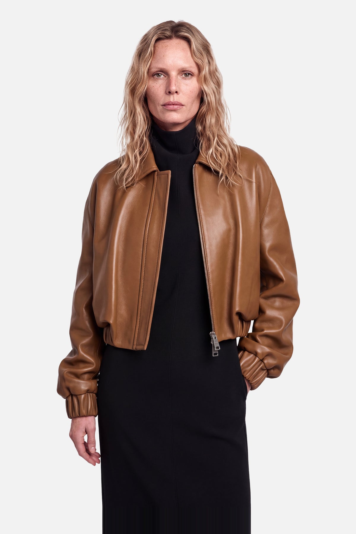 Cognac leather bomber jacket, front view, worn by model, black turtleneck dress.