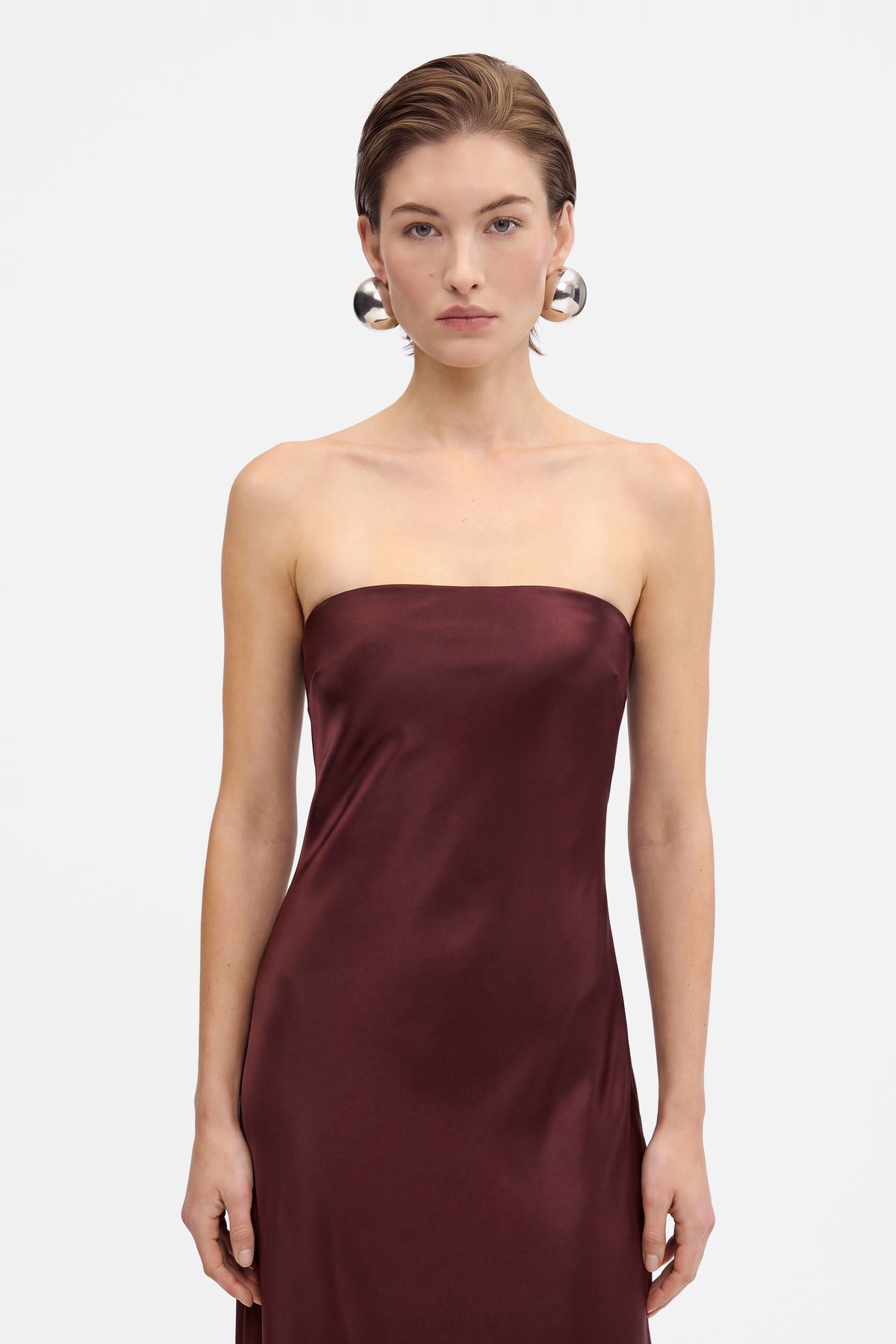 Burgundy strapless slit gown, close-up front view, model wearing silver earrings.