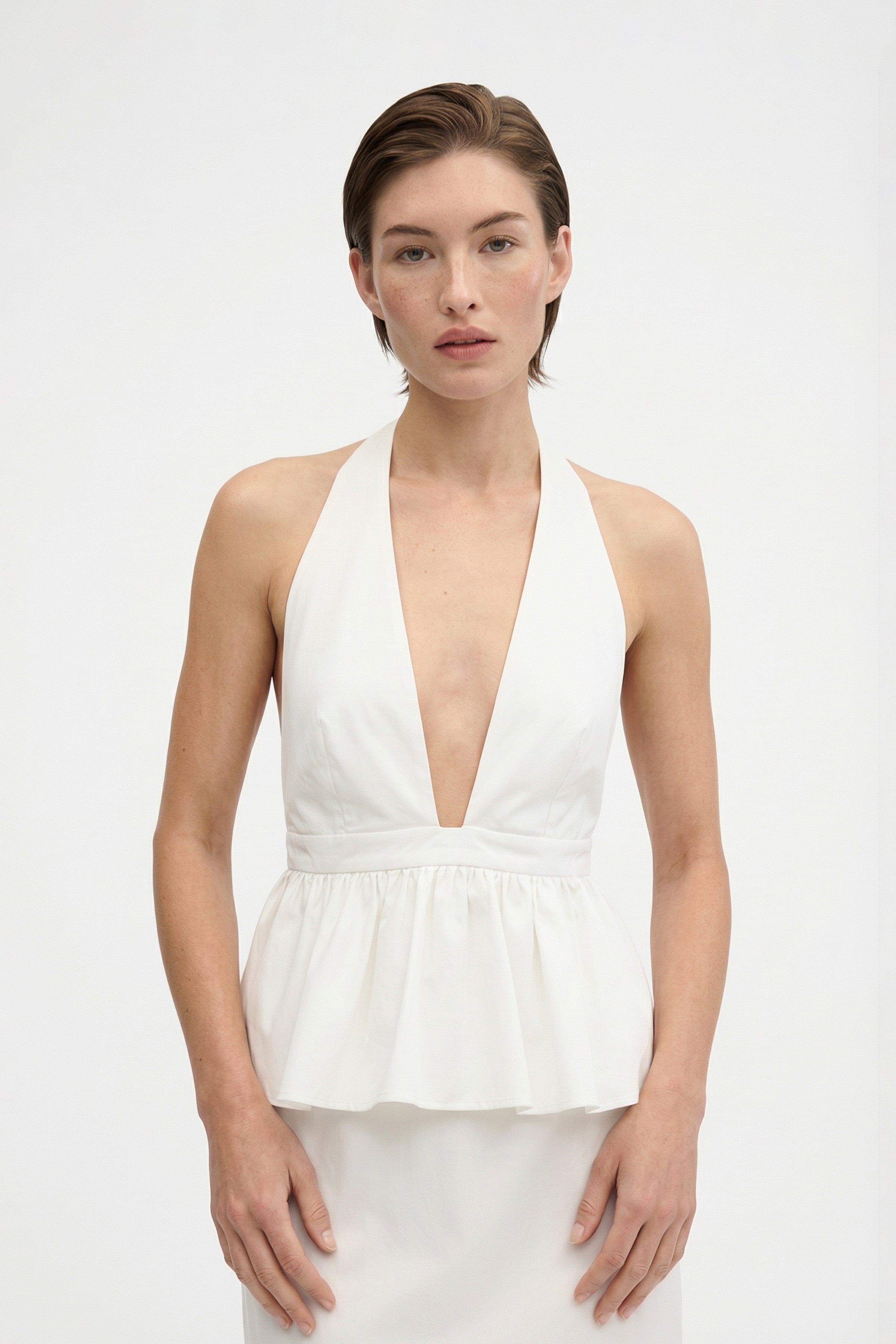 Front view of model wearing a white halter peplum dress against a plain background.