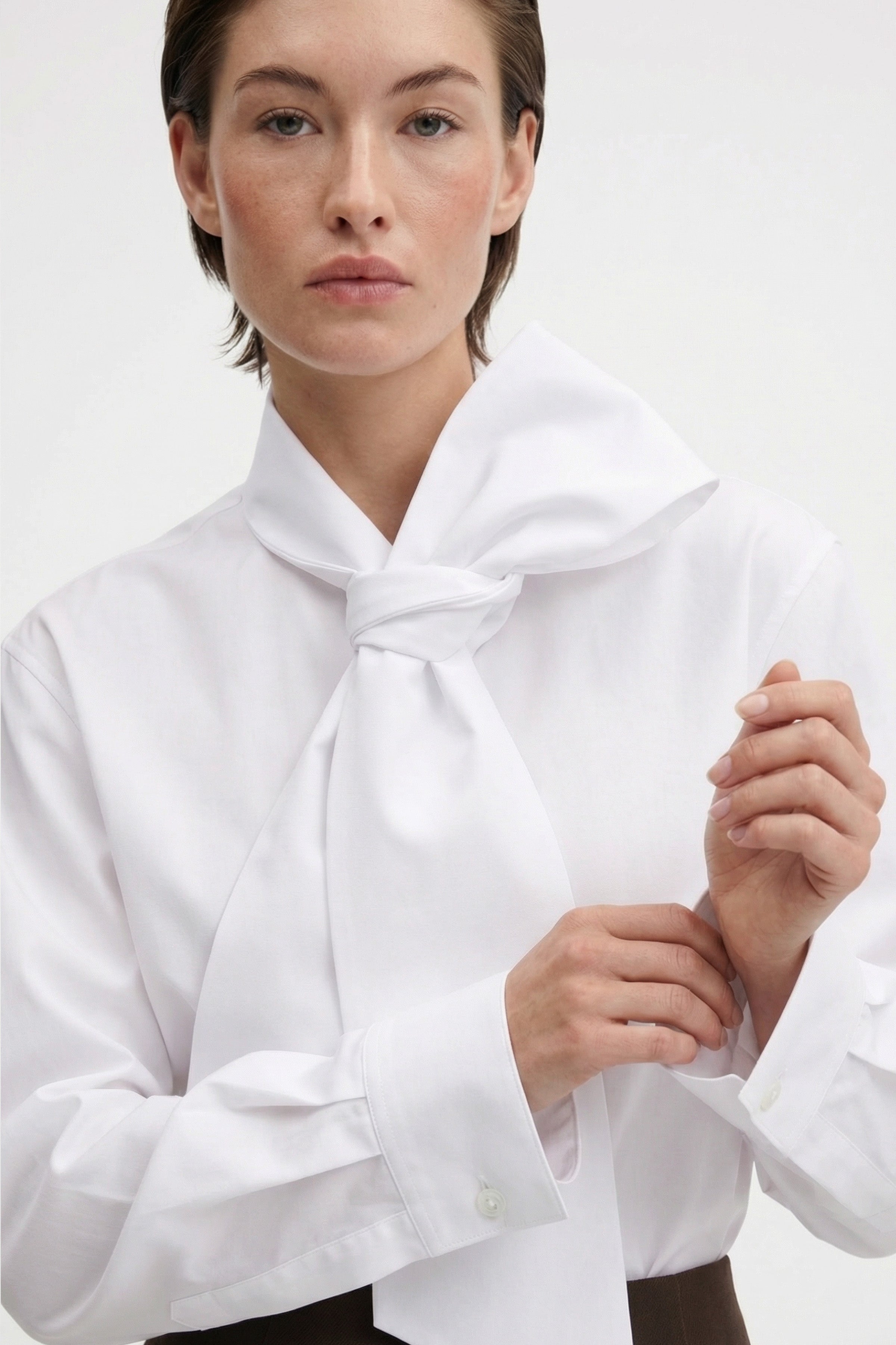 Model in elegant white blouse with large bow, buttoned cuffs. Front view.