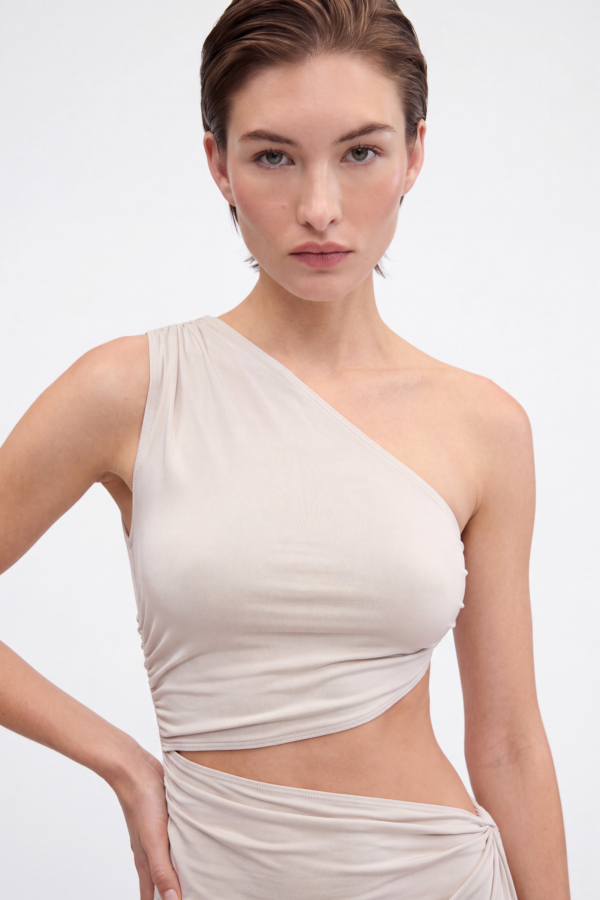 Model in cream asymmetric cutout maxi dress, front view, showing shoulder and waist detail.