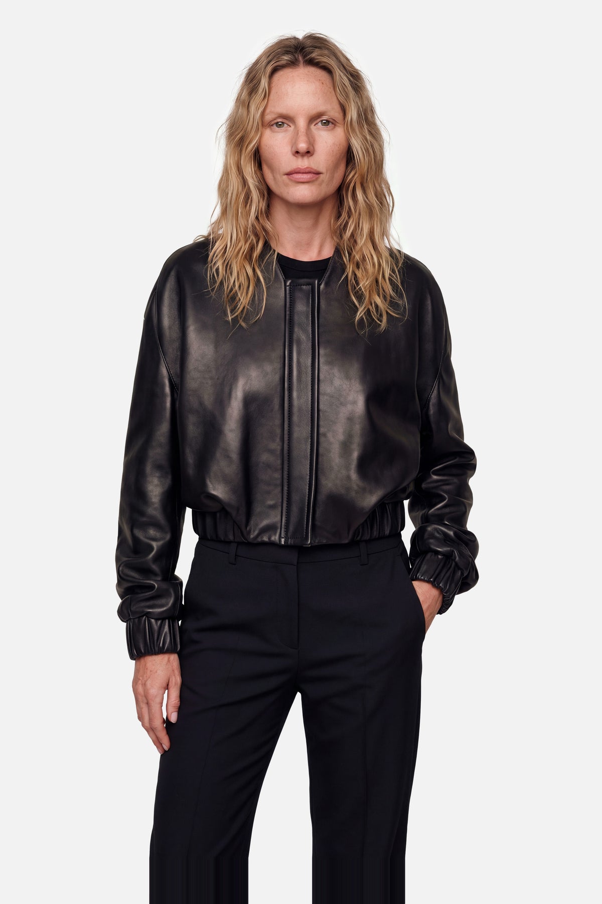 Front view of black leather bomber jacket, worn by model, hands in pockets.