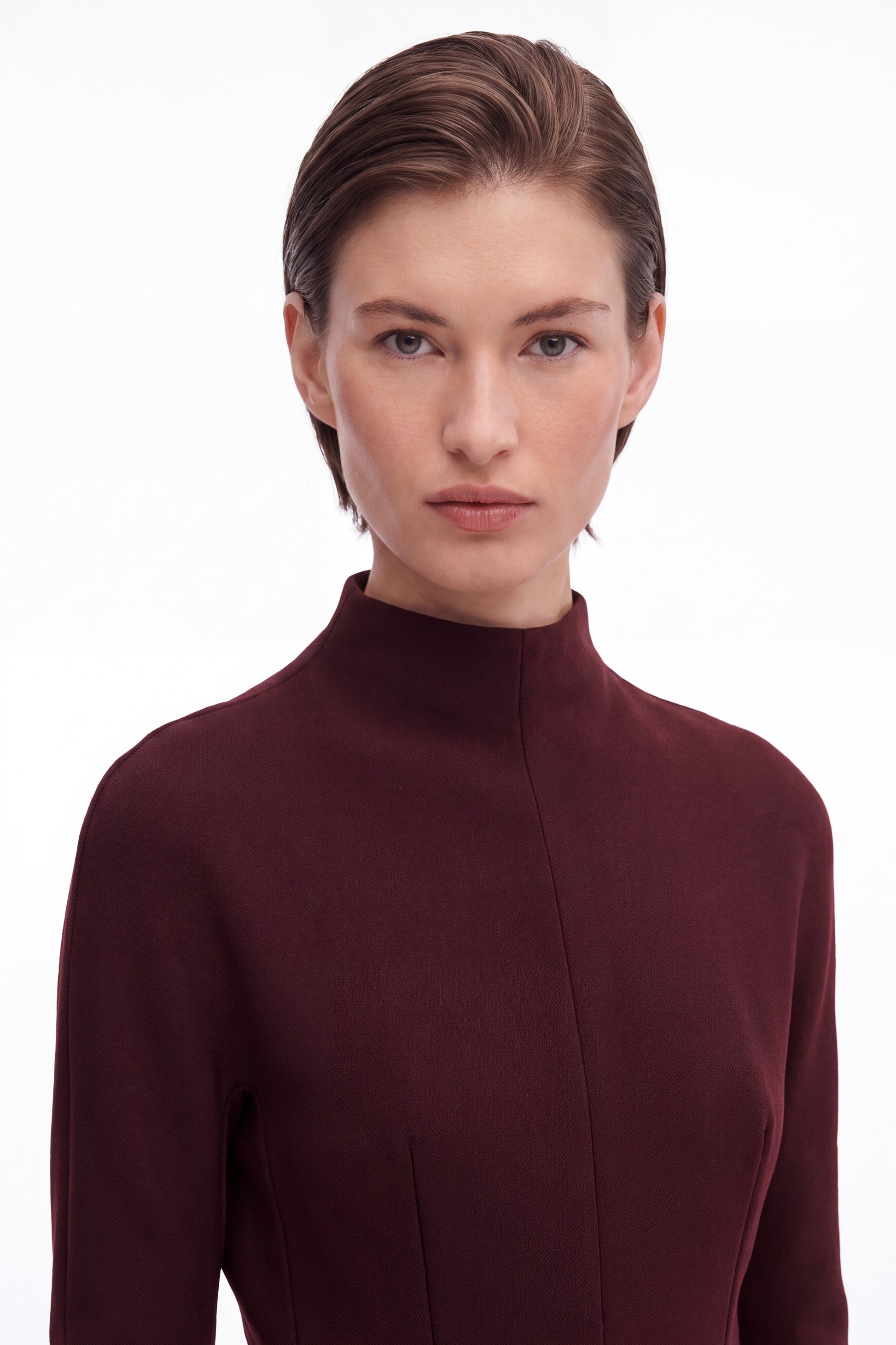 Close-up front view of burgundy structured mini dress with high neckline on model.