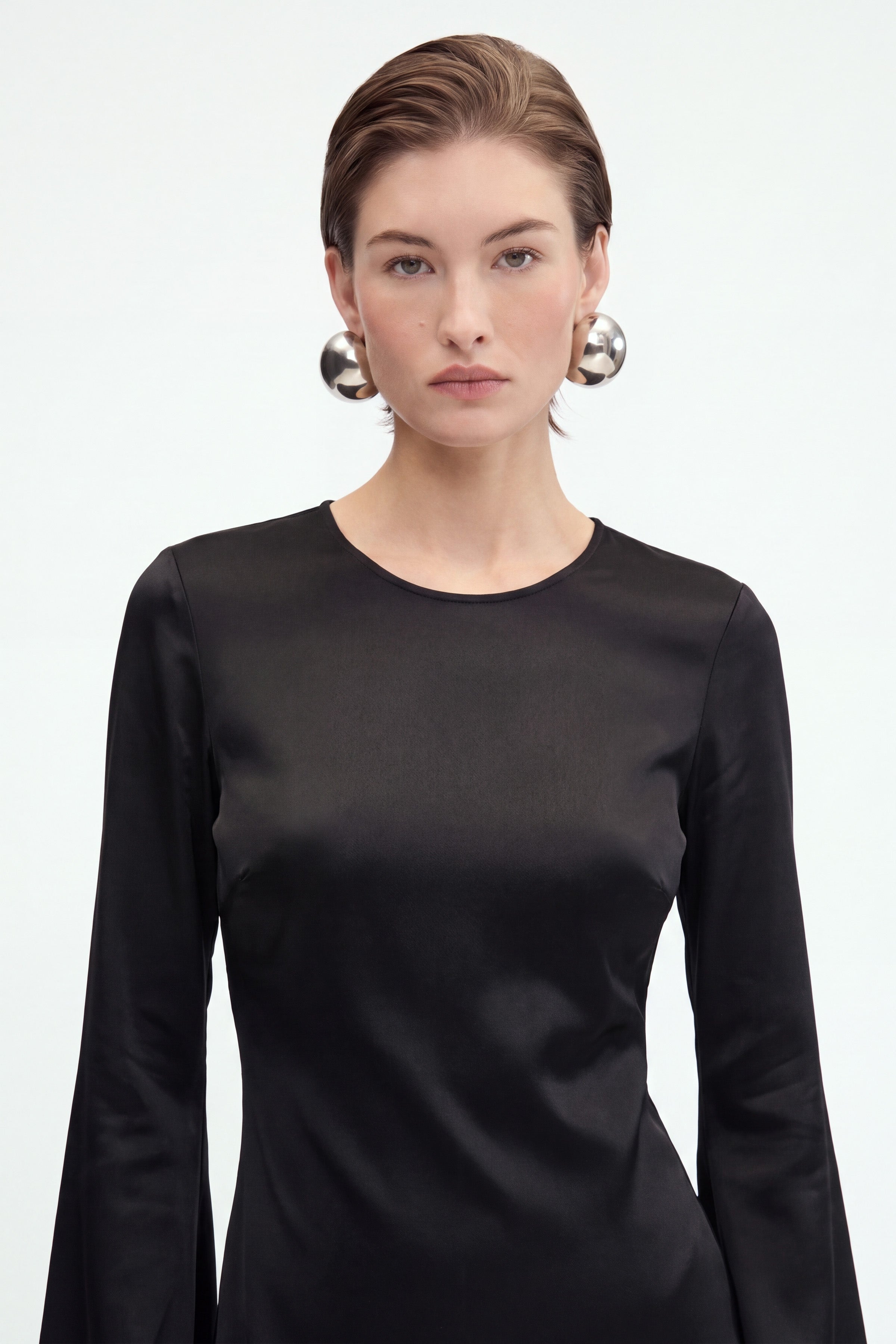 "Front view of black satin dress with flare sleeves, worn by model with silver earrings."