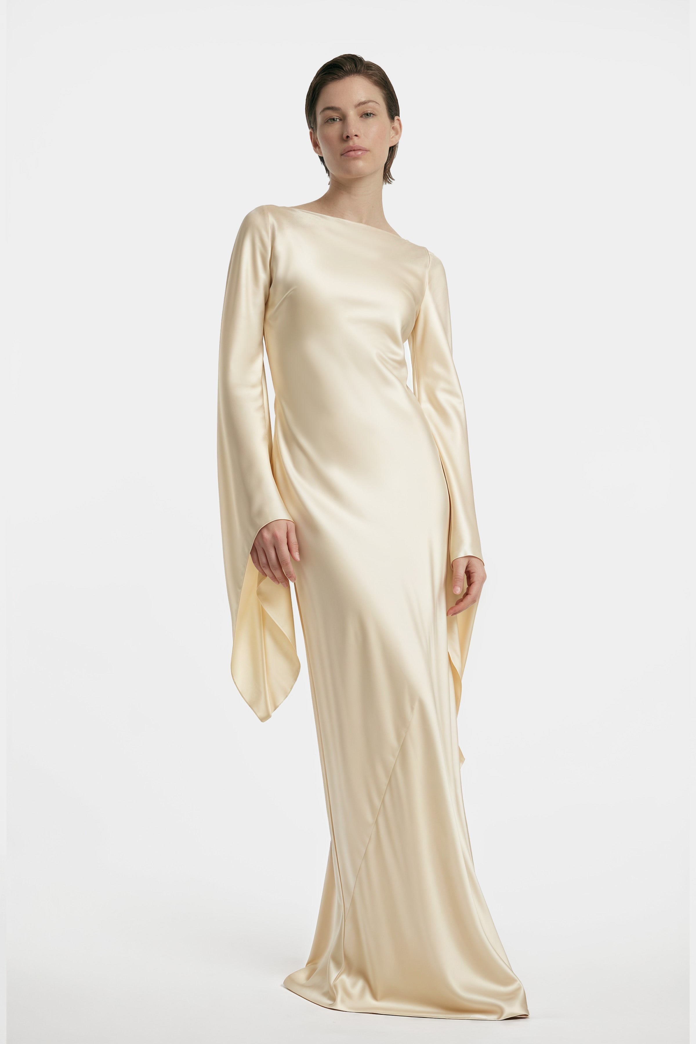 Model wearing elegant, long-sleeved golden silk gown with flowing silhouette, front view.