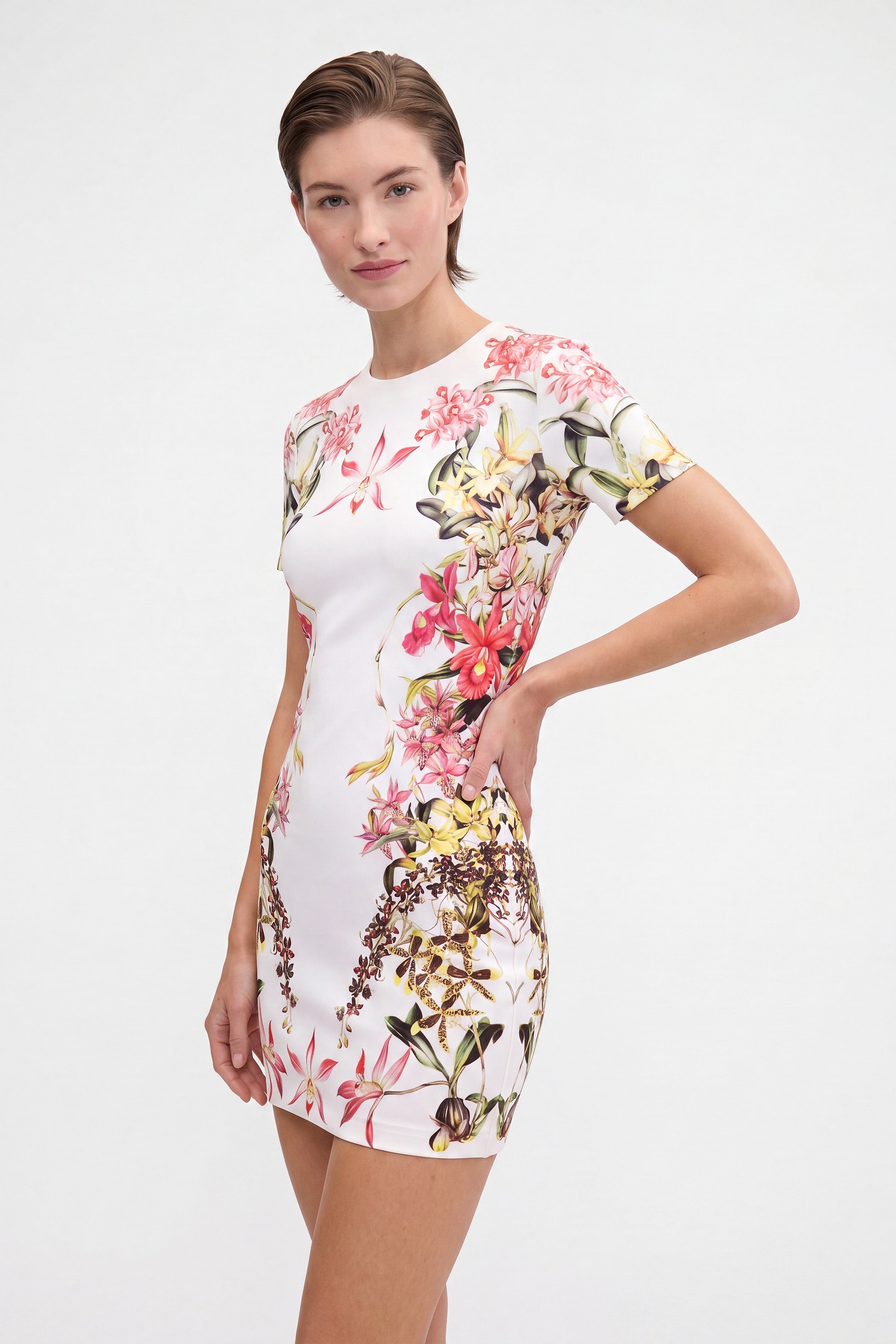 Front view of model wearing a floral print jersey mini dress, hand on hip.