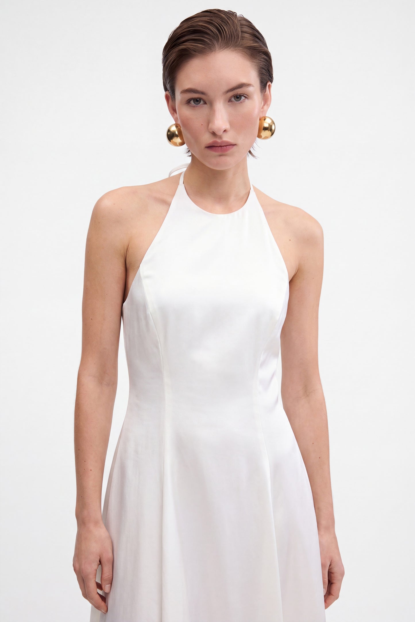 Front view of a white halter midi dress on a model with golden earrings.
