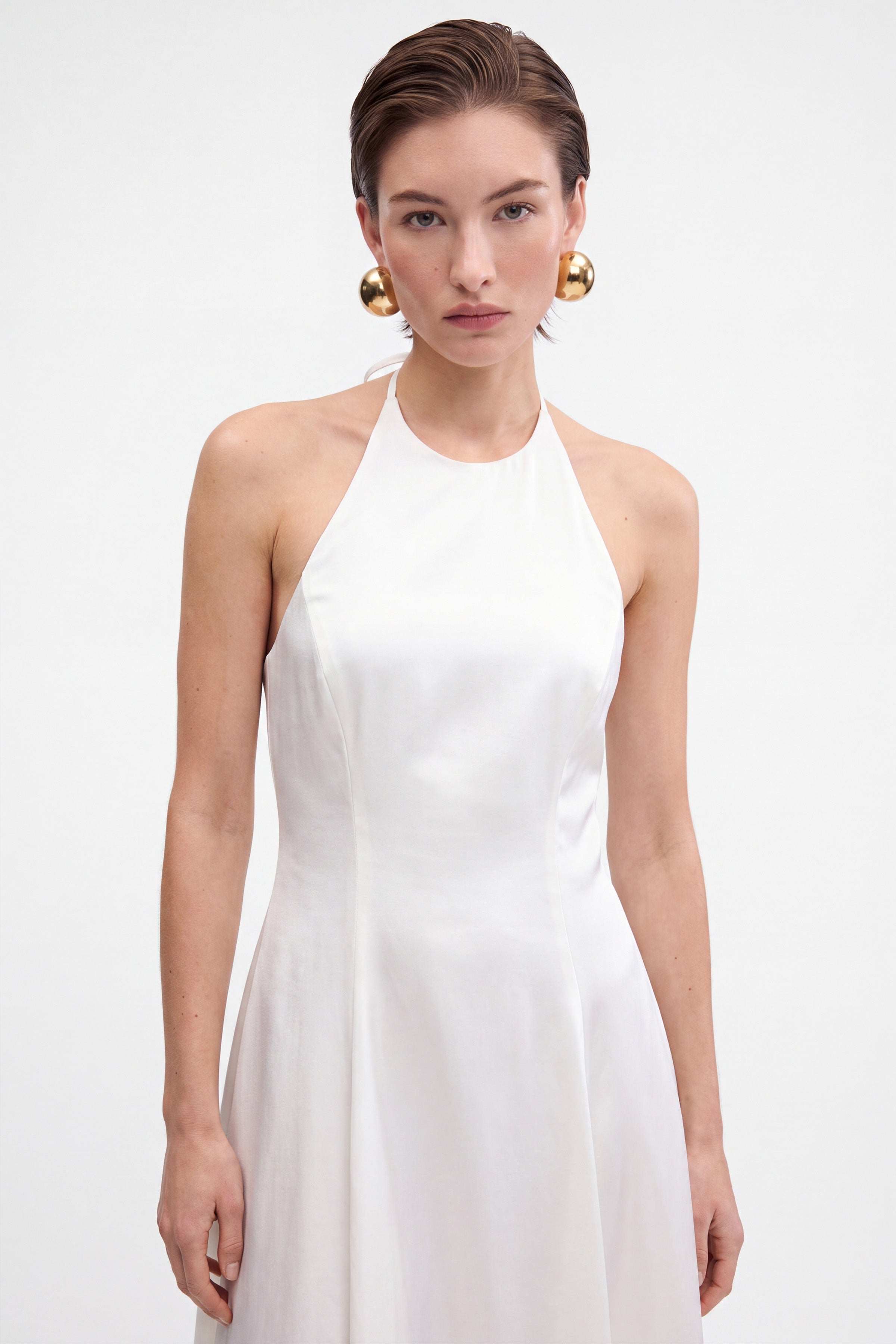 Front view of a white halter midi dress on a model with golden earrings.
