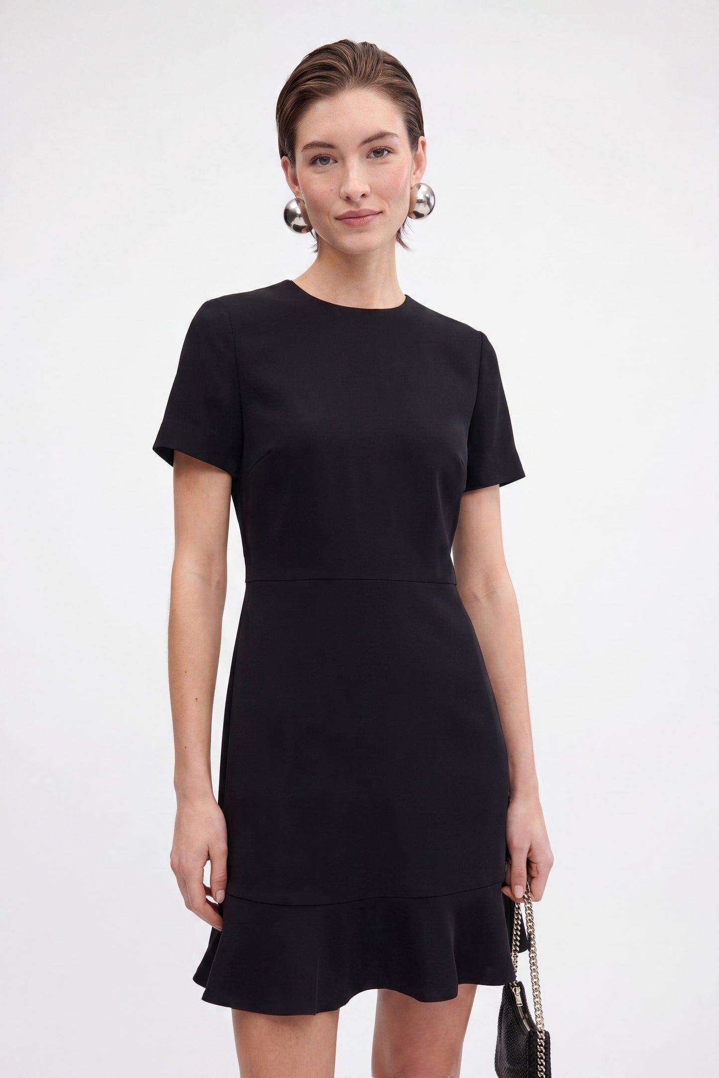 Model wearing black ruffle hem dress, front view, short sleeves, minimalistic style.